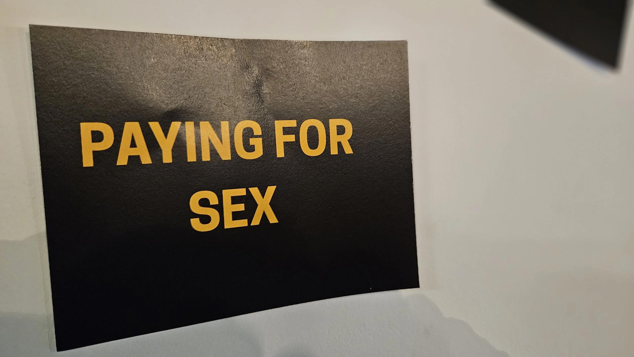 Black poster with yellow text that reads 'PAYING FOR SEX'