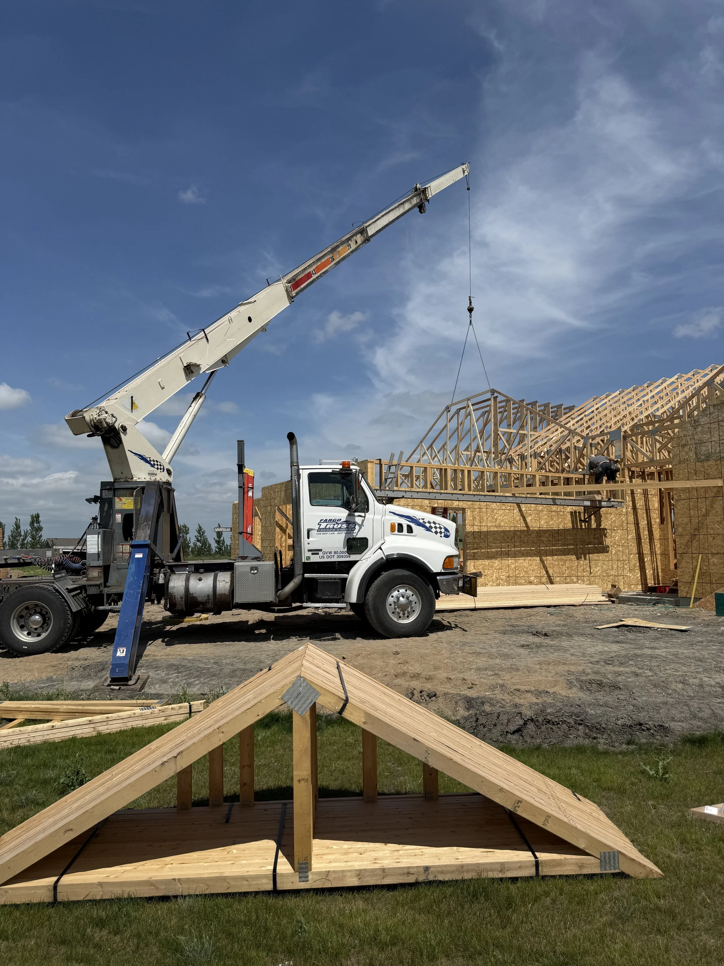 Construction site with a crane lifting framing wood for a building with a wooden framework and workers assembling it.