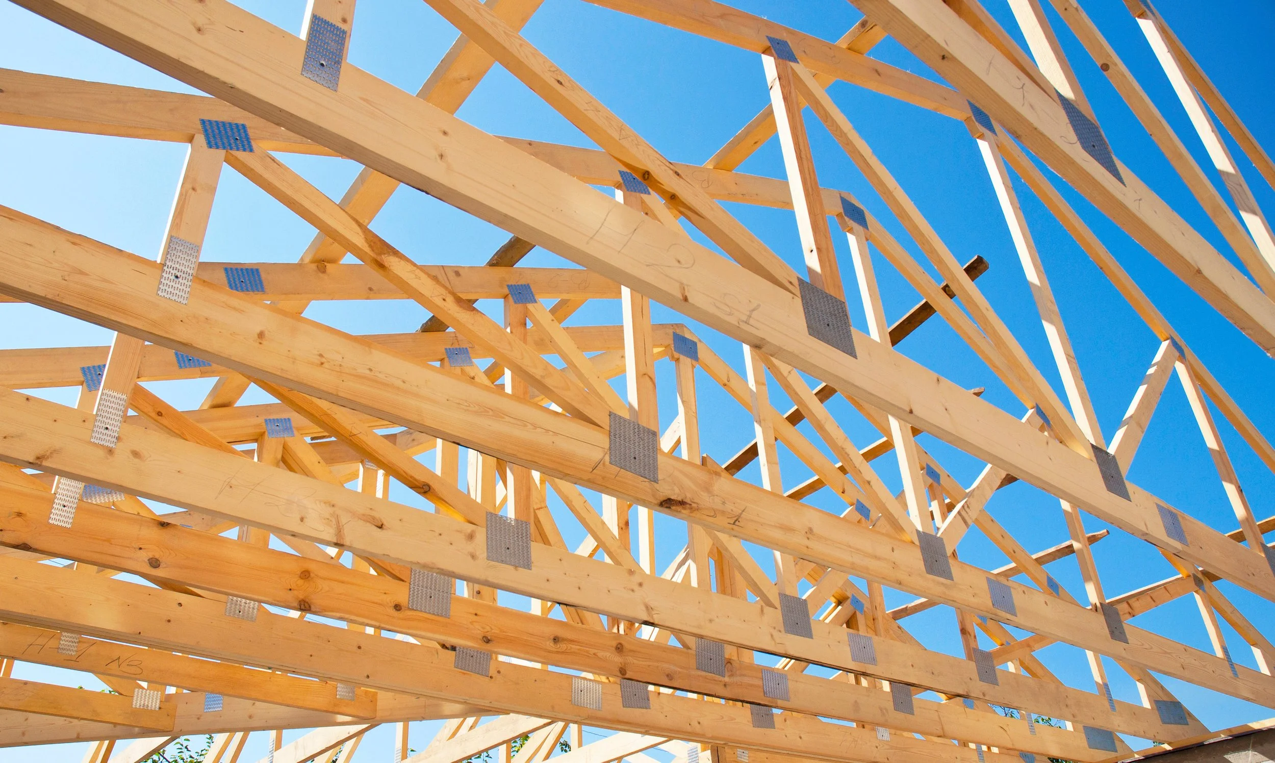Wooden framing structure for a building under construction against a clear blue sky.