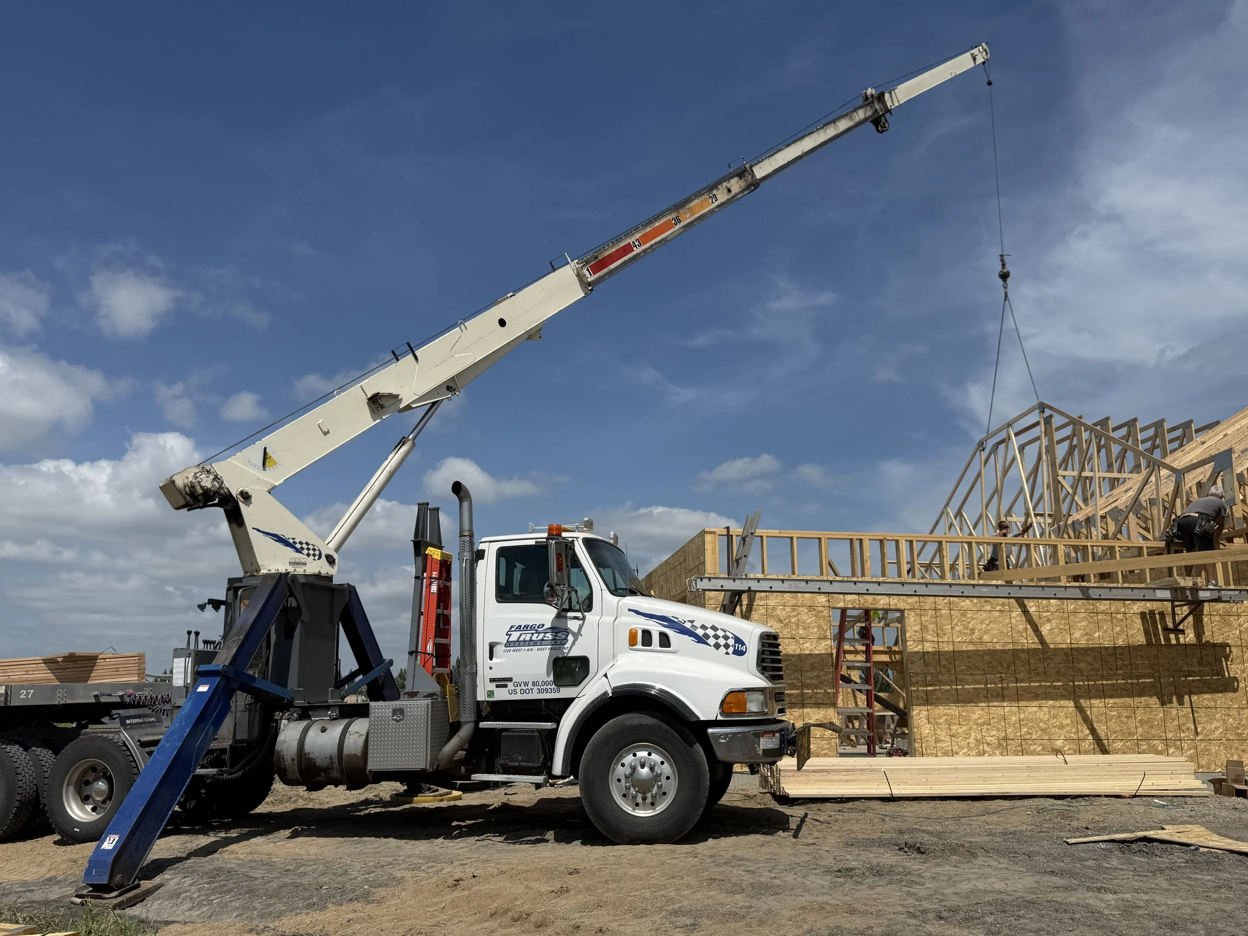 A white crane truck lifting a wooden structure at a construction site under a partly cloudy sky.