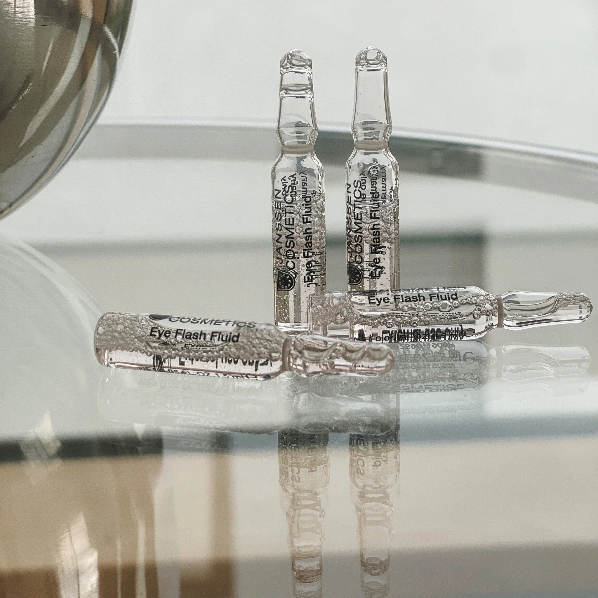 Four small glass ampoules labeled 'Eye Flash Fluid' placed on a reflective surface, with some ampoules standing upright and others lying down.