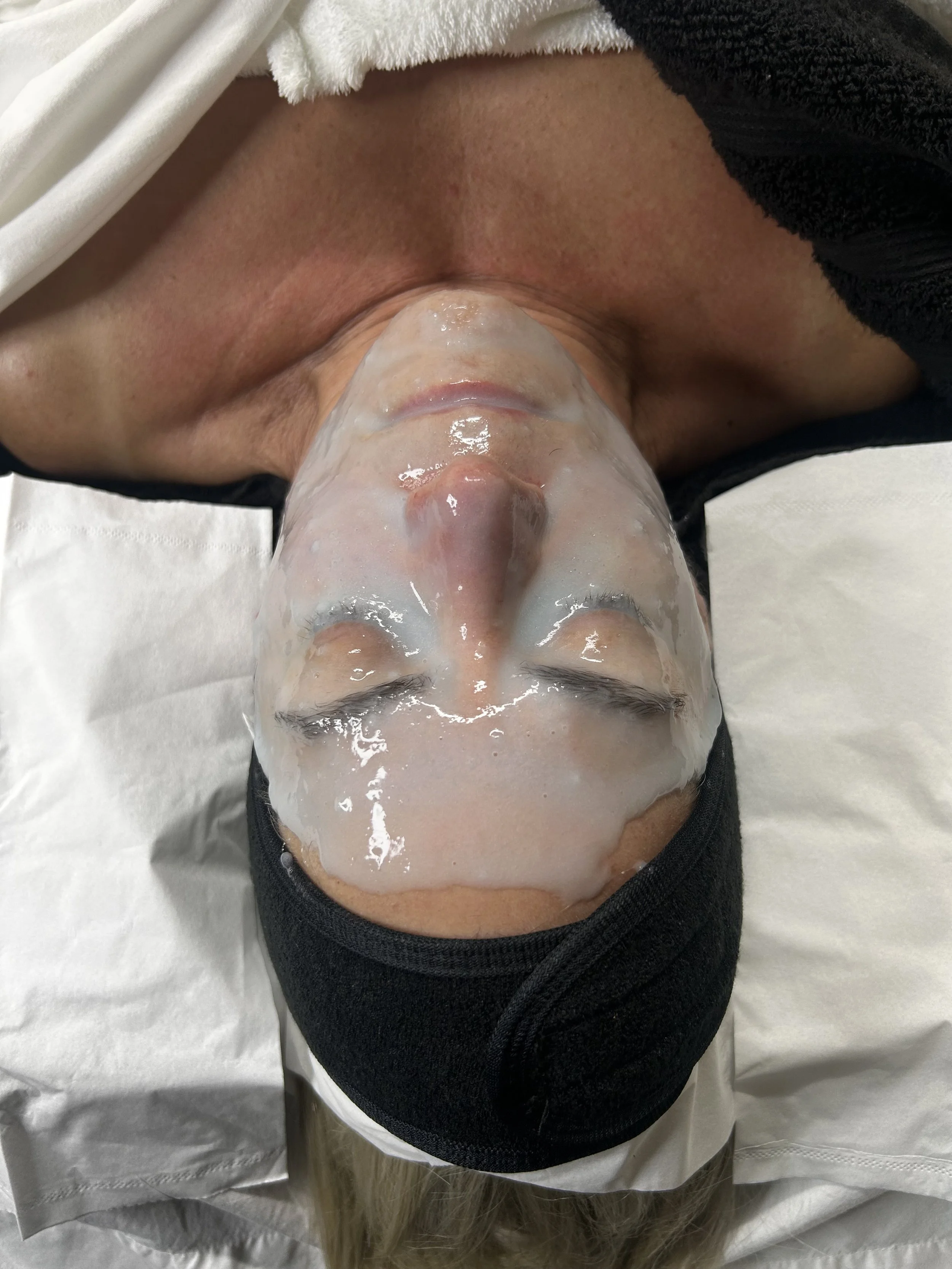 Person lying down with a facial mask and eye cover, eyes closed.