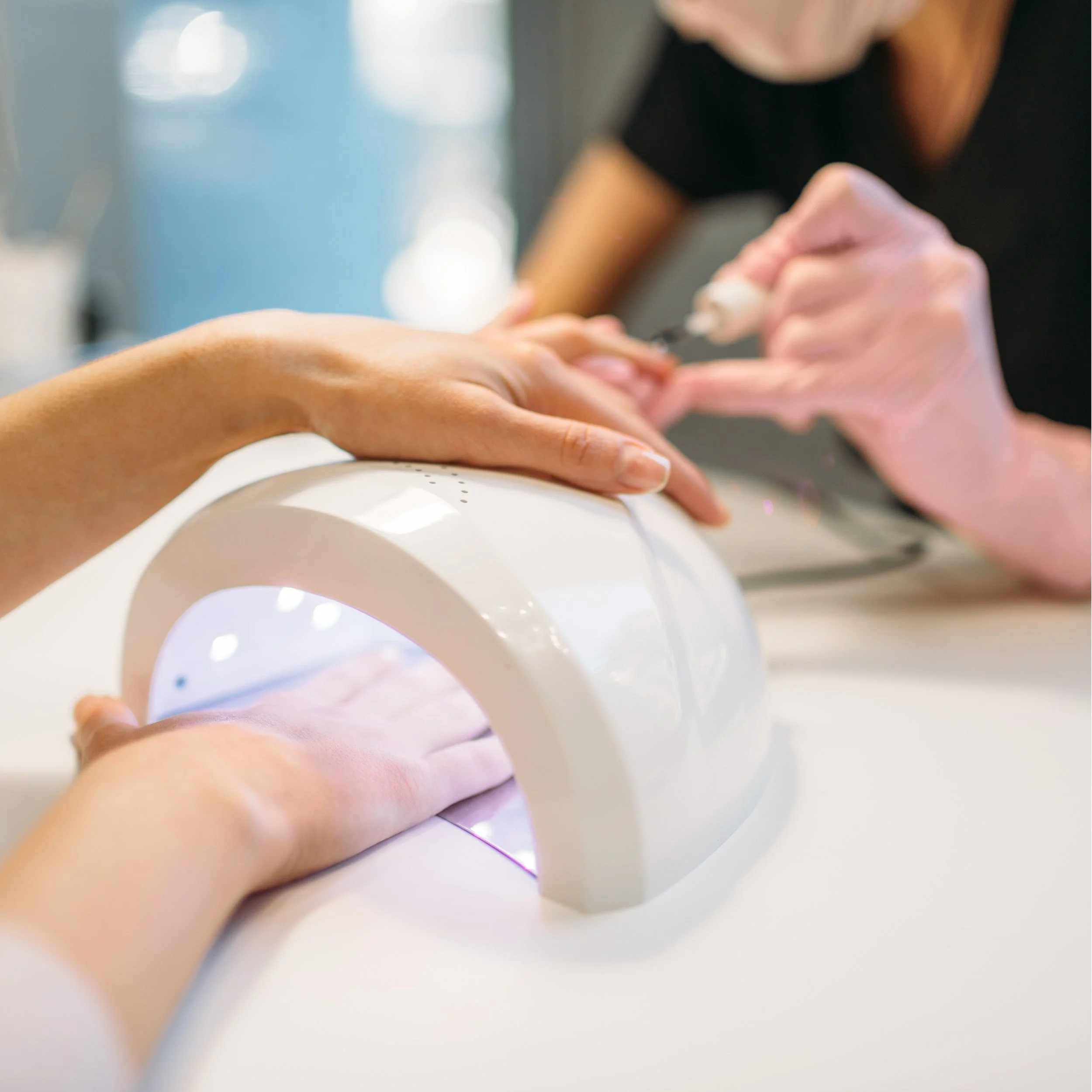 Nail technician applying white nail polish to a client’s fingernails using an ultraviolet light curing lamp.