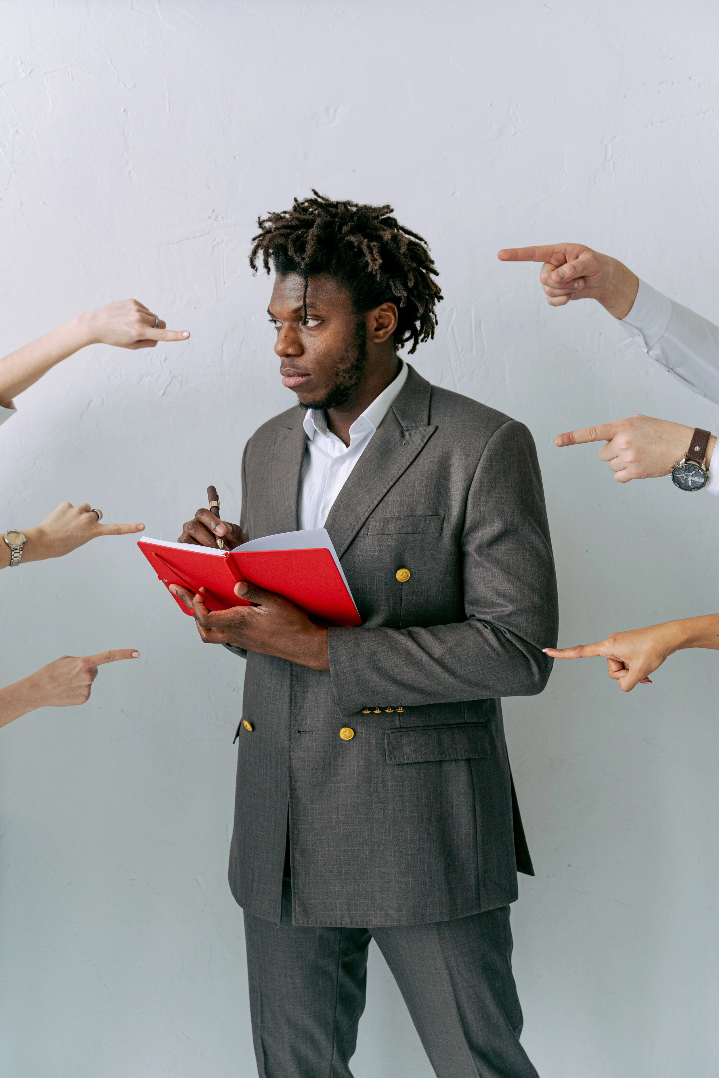 Man in a business suit holding a notebook surrounded by arms pointing toward him