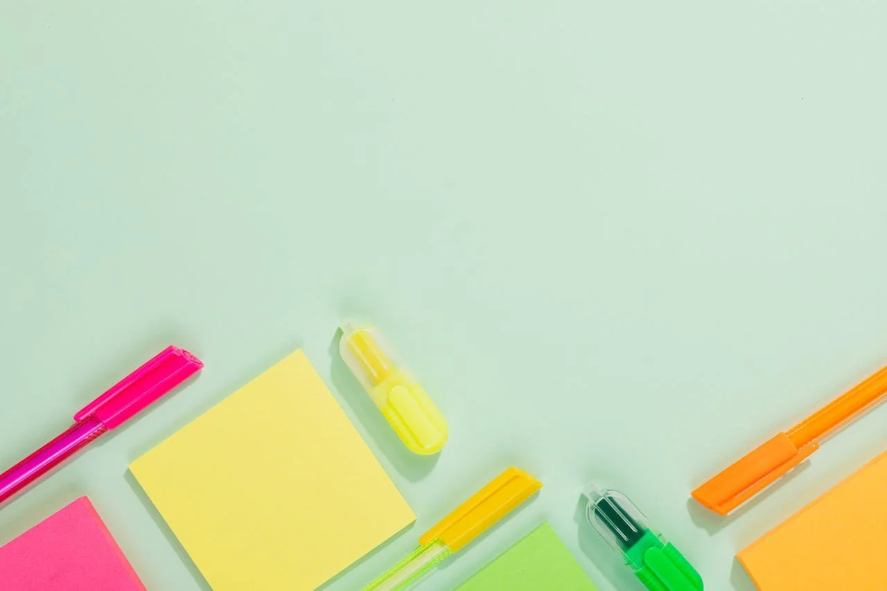 Colorful highlighters, sticky notes, and markers arranged on a light green surface.