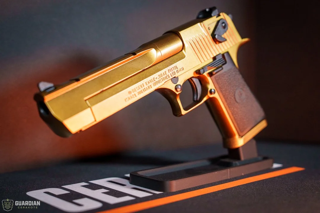 A gold and black Desert Eagle pistol on display, mounted on a stand with the word 'GEEKO' visible on a mat underneath.