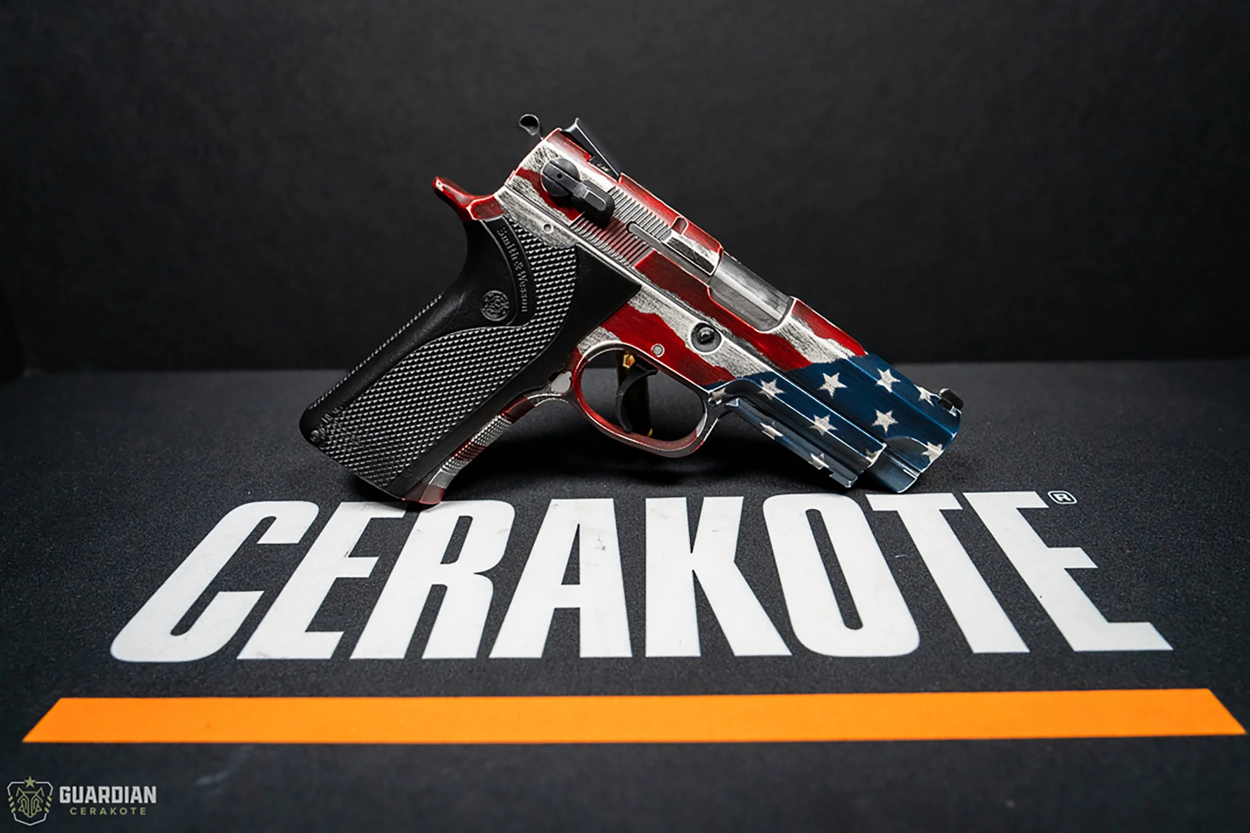 A handgun with an American flag design on its body, resting on a black surface with the word 'CERAKOTE' printed on it in large white letters.