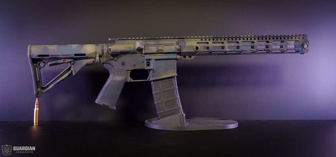 A modern rifle with a camouflage finish, mounted on a display stand, with a bullet placed underneath the stock.