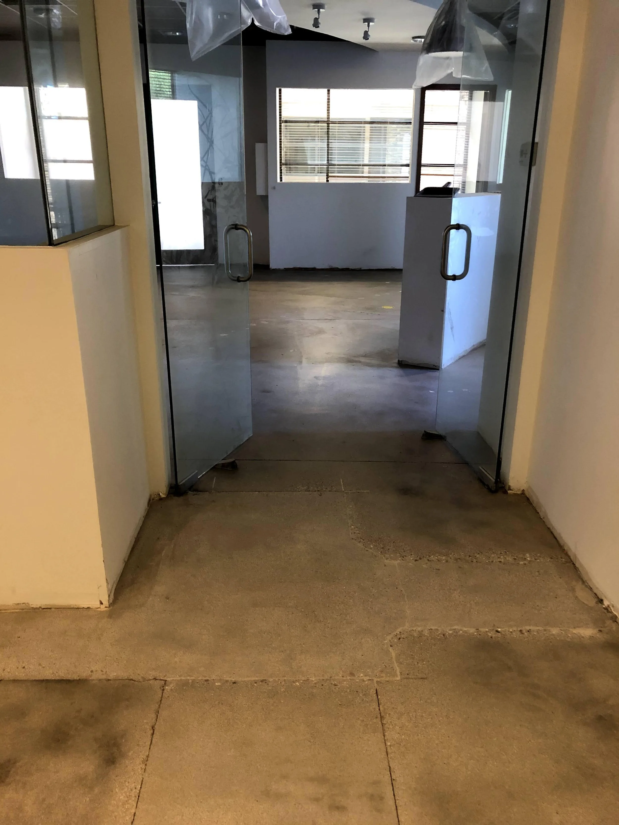 Inside view of a hallway with glass doors and a window, showing a room with blinds and scattered objects on the floor.