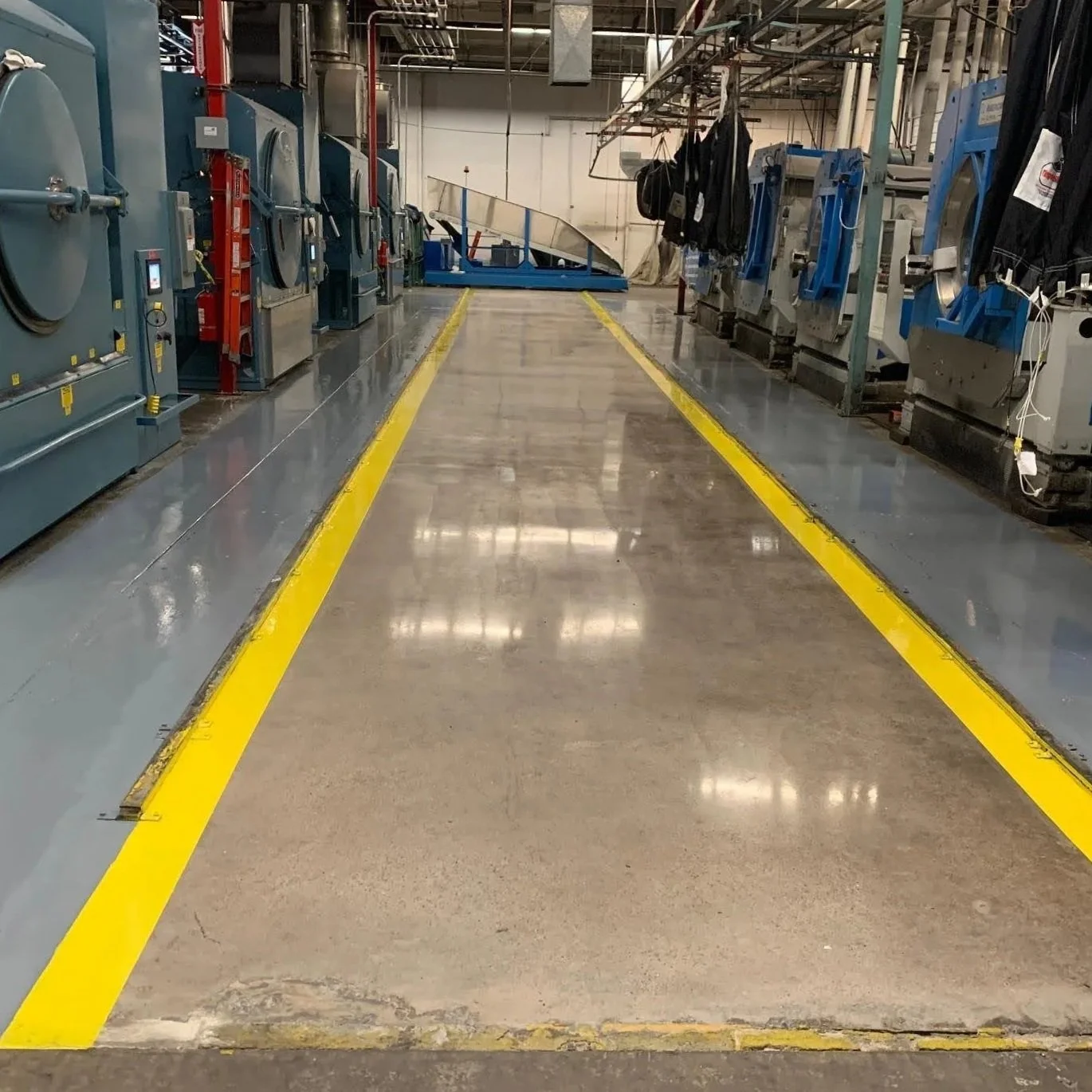 Industrial laundry facility with laundry machines on both sides, a smooth concrete floor, and yellow safety lines marking pathways.