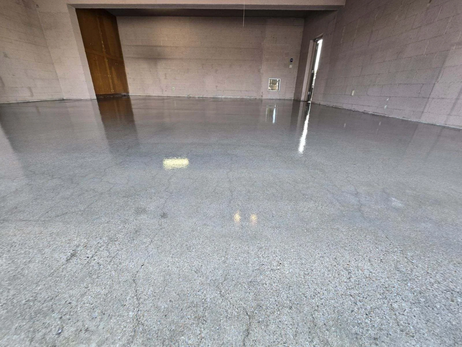 A finished concrete floor in an indoor space with brick walls and a doorway leading outside.
