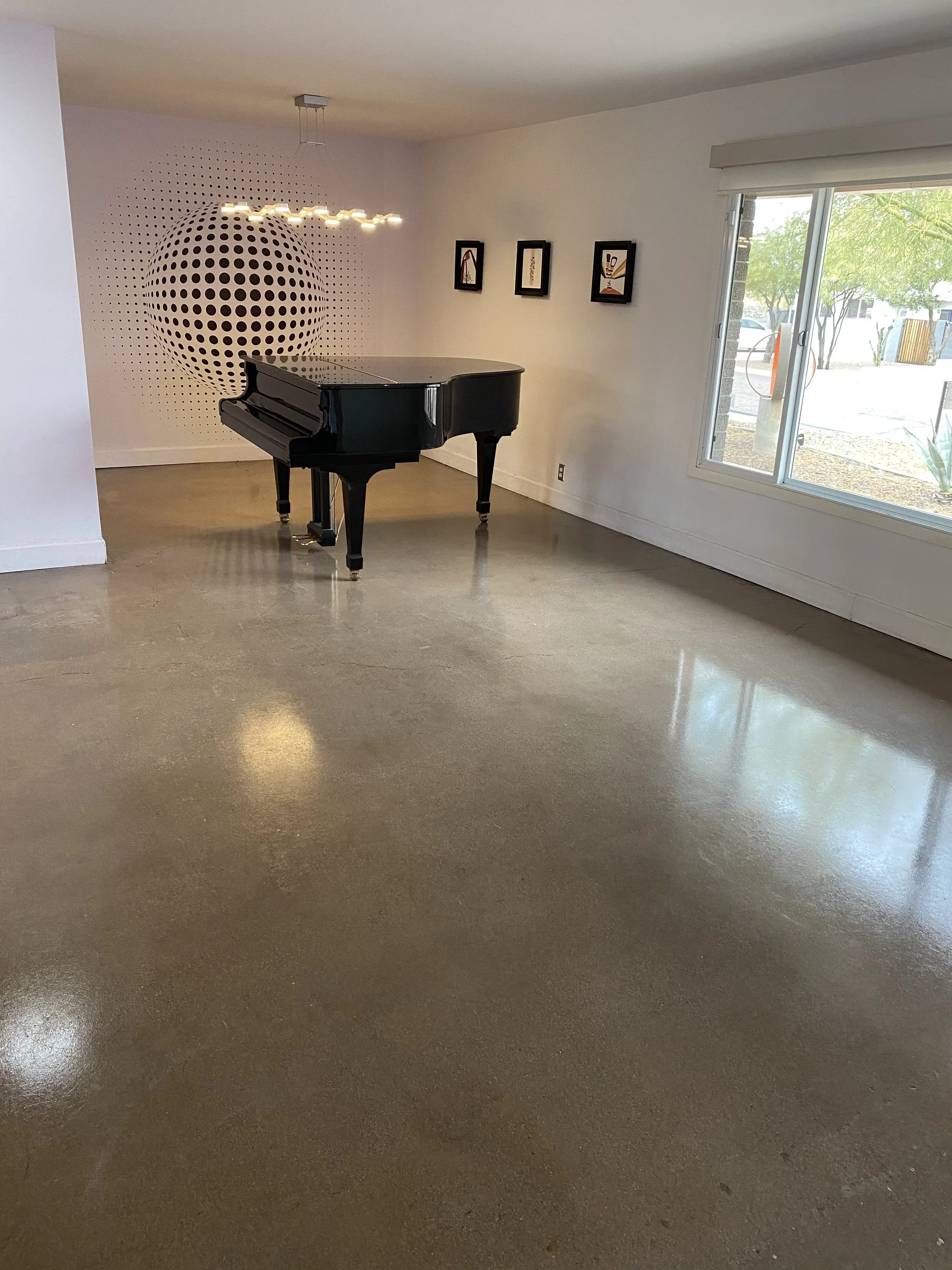A black grand piano in a minimalistic room with white walls, a large window, and modern artwork on the wall, featuring a geometric black and white art piece on the back wall.