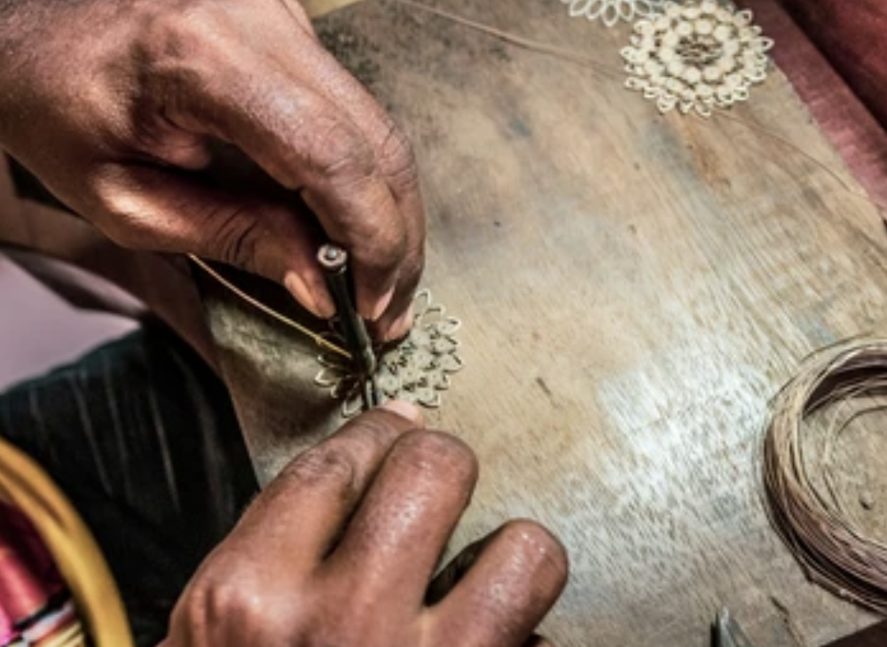 Hands working on intricate wire jewelry on a wooden surface.