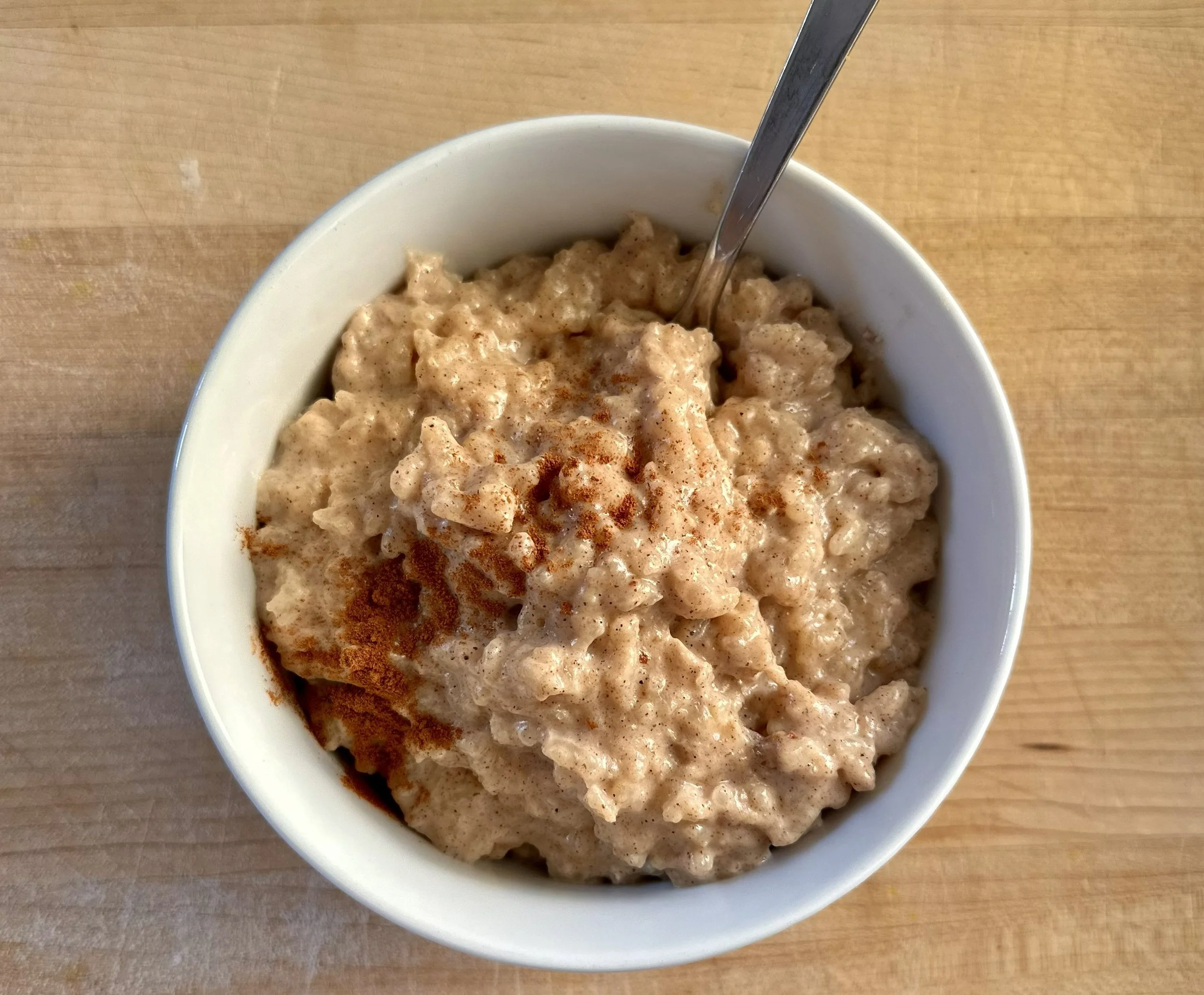 A white bowl filled with creamy rice pudding sprinkled with cinnamon on a wooden surface.