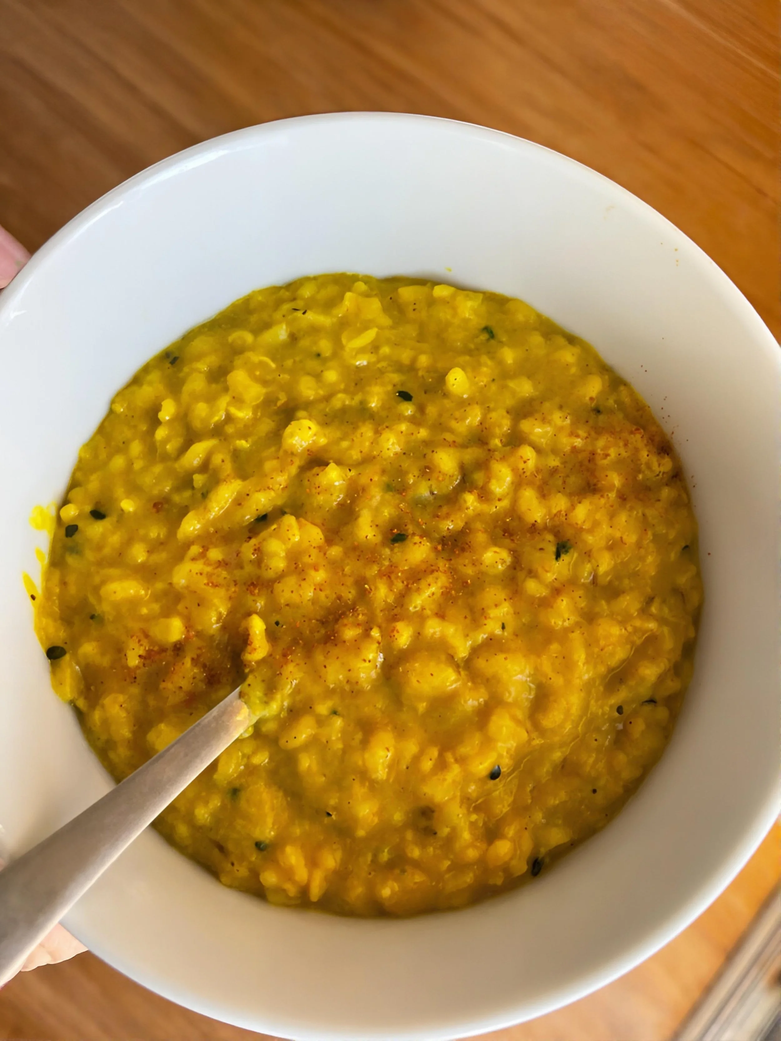 A bowl of Kitchari soup with a spoon inside, resting on a wooden surface.