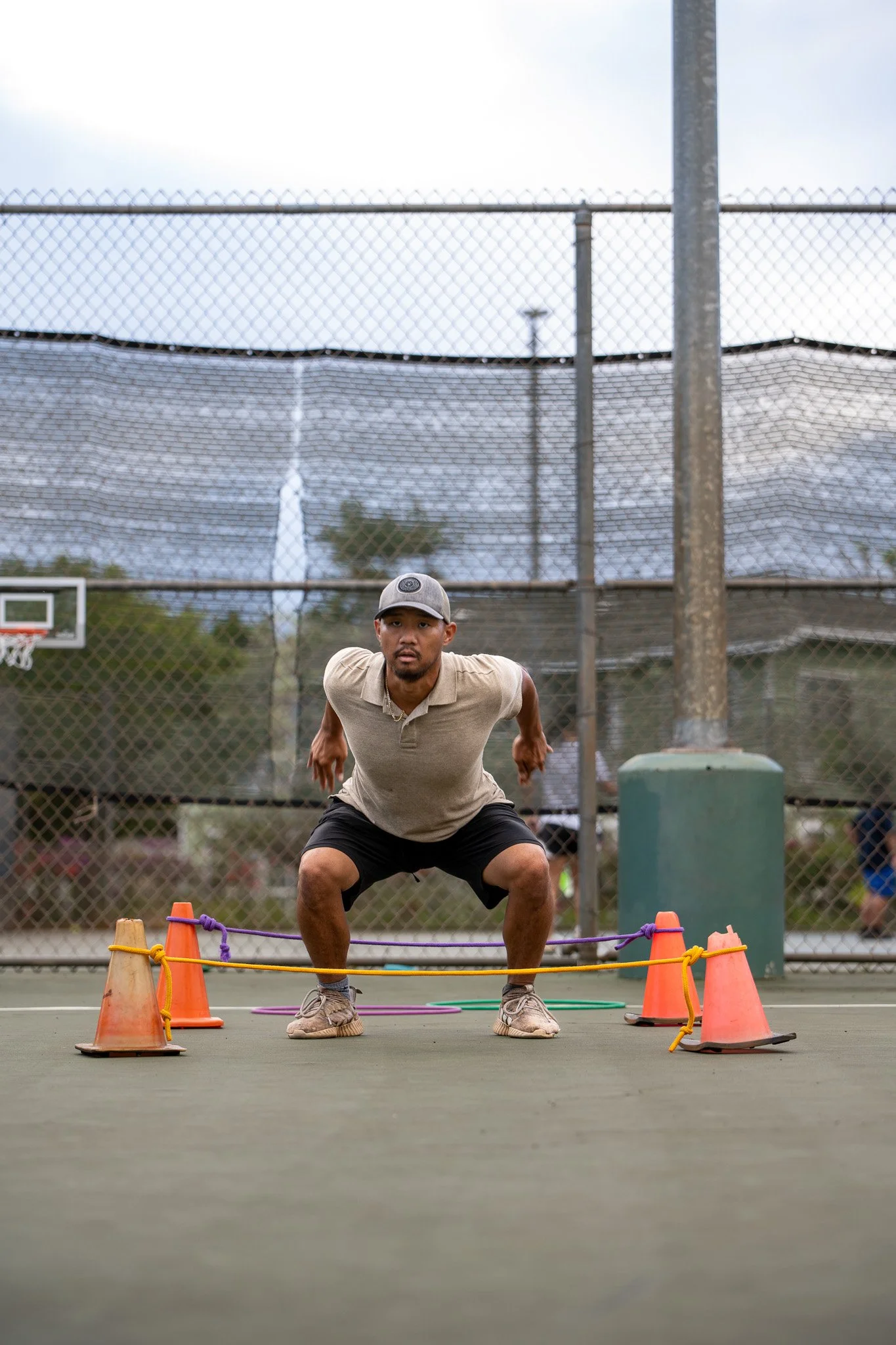 Man performing squat exercise on a tennis court with cones.