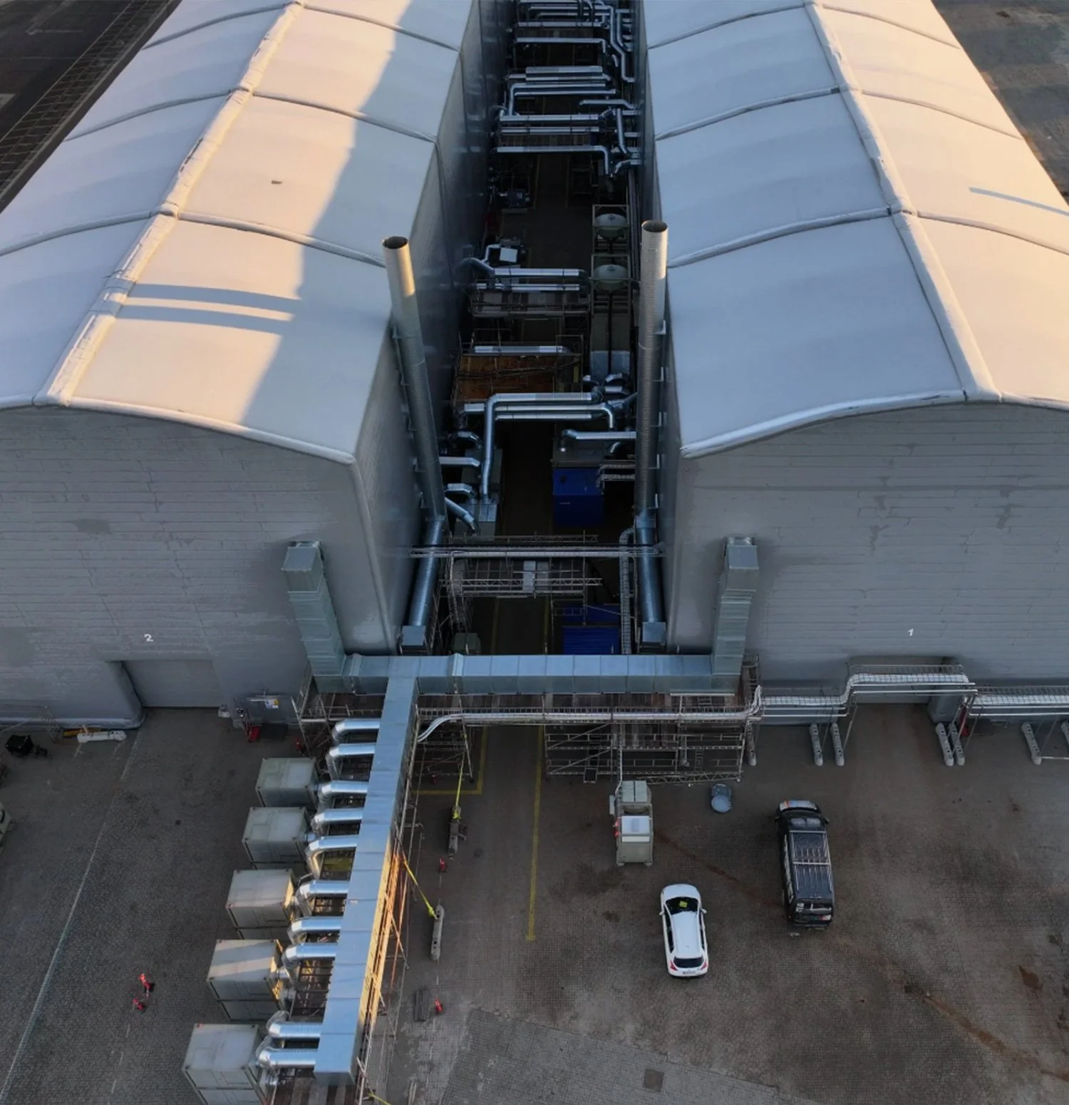 Aerial view of an industrial building with a large, curved roof and visible ventilation and piping systems on the exterior and interior.