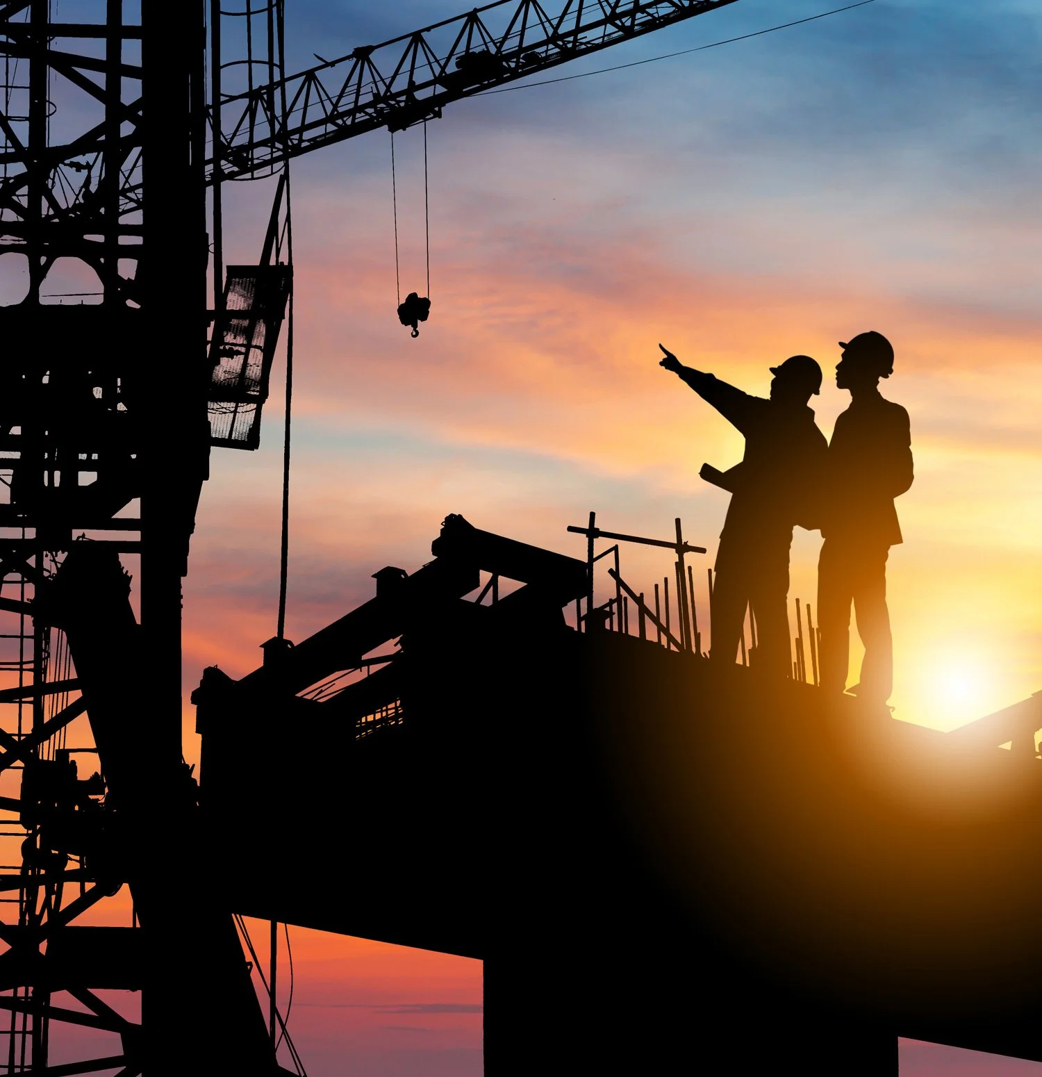 Silhouettes of construction workers on a building site at sunset, with a crane in the background and the sky with orange, pink, and purple hues.