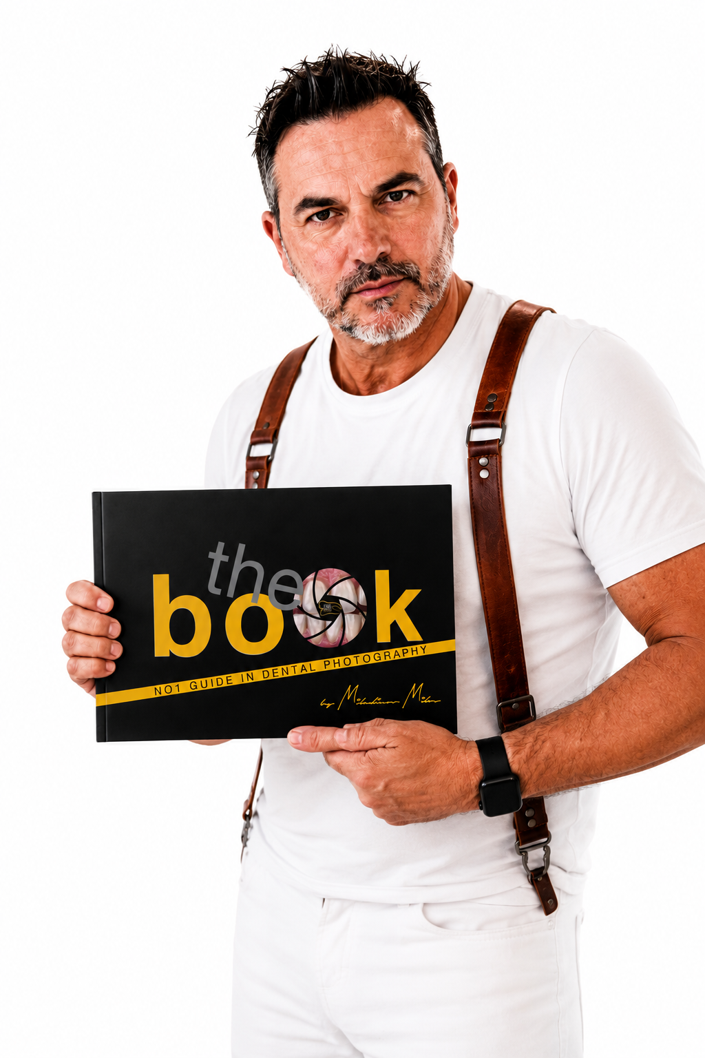 Man with glasses and a beard holding a book titled 'the book' about dental photography, wearing a white t-shirt, suspenders, and a fitbit watch, against a white background.