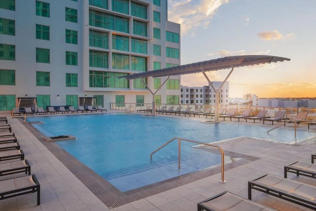 Empty rooftop pool area surrounded by lounge chairs, with a city skyline at sunset in Dania Beach