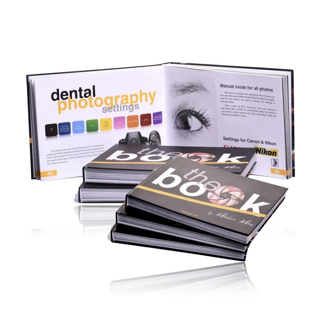 Stack of photography books and an open book on photography settings, with focus on dental photography, featuring camera diagrams and an eye illustration.