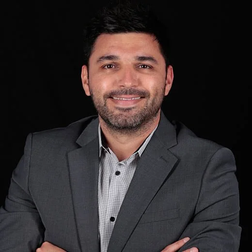 A professional man smiling in a business suit against a black background.