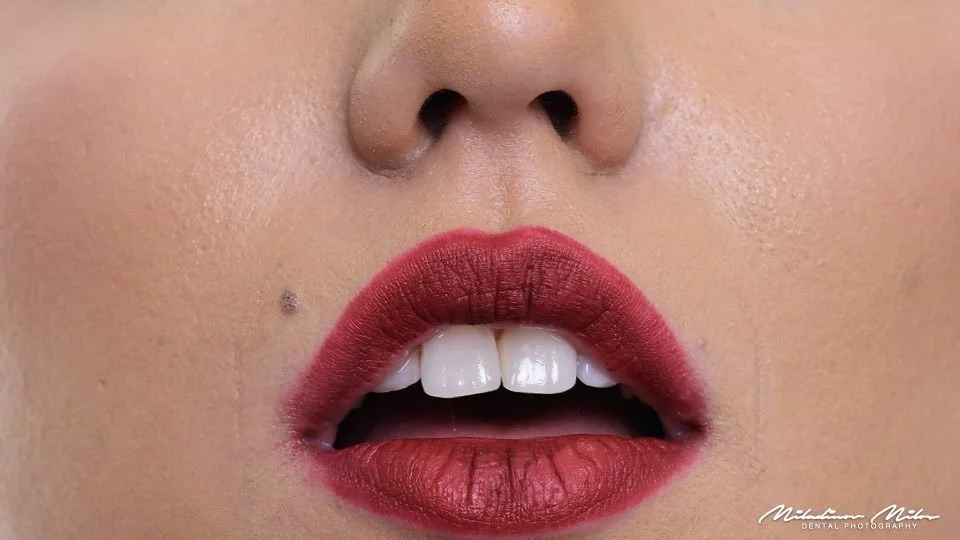 Close-up of a woman's face showing lips with dark red lipstick and her slightly open mouth exposing white teeth.
