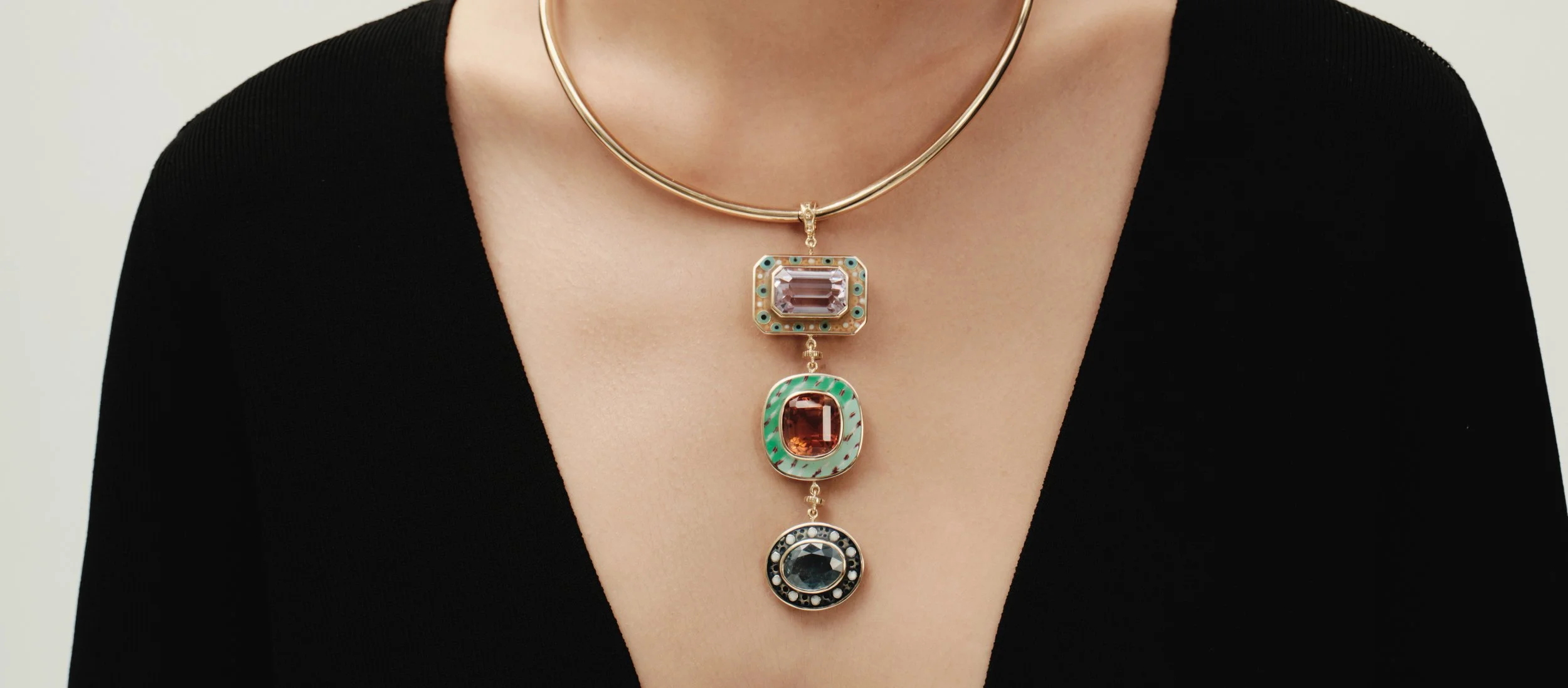 Close-up of a woman's neck and chest, wearing a gold statement necklace with four colorful, rectangular-shaped gemstone pendants layered vertically.