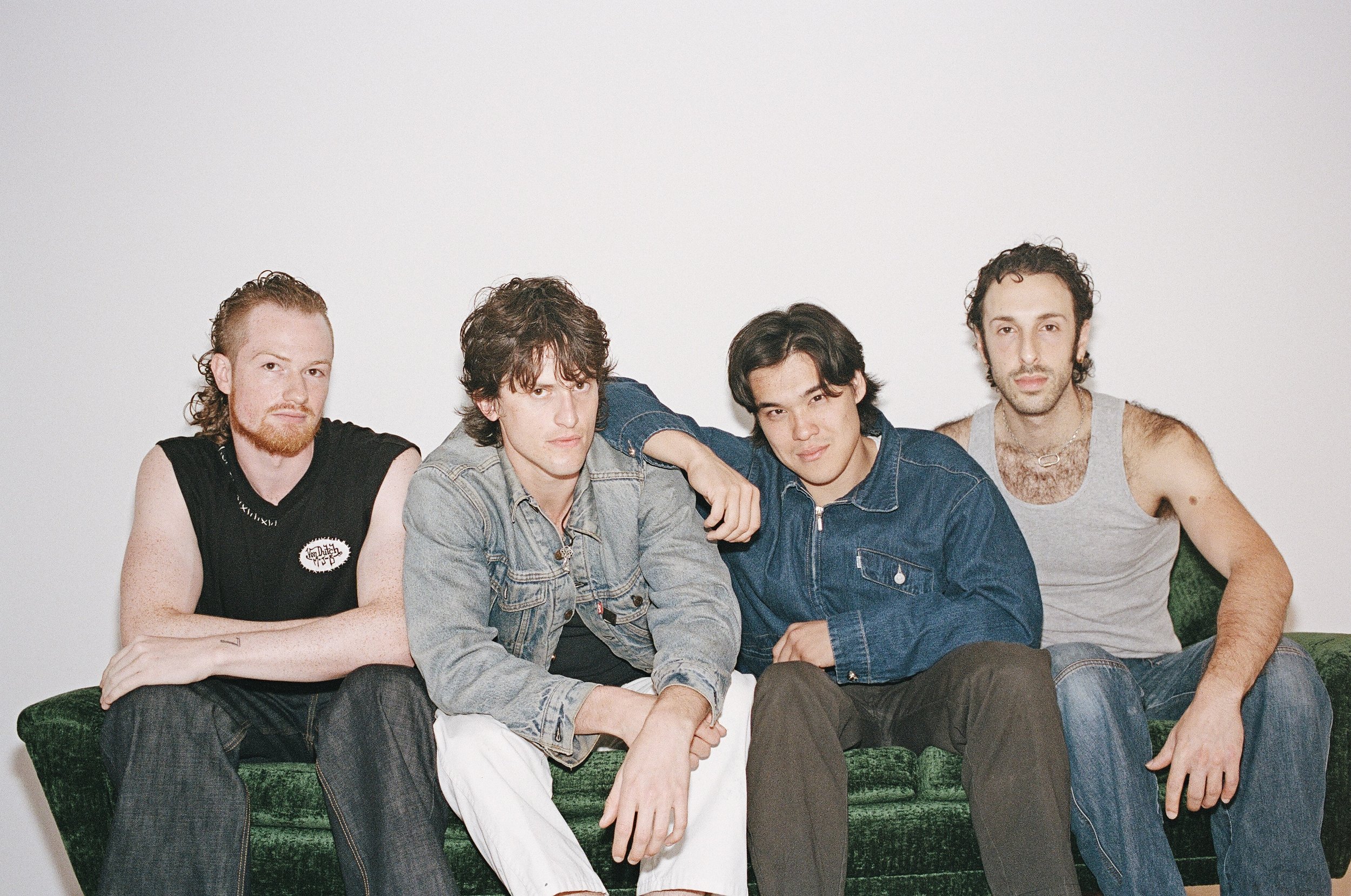 The four young men of Telescreens lounge low on a green velvet sofa, white wall framing them from above