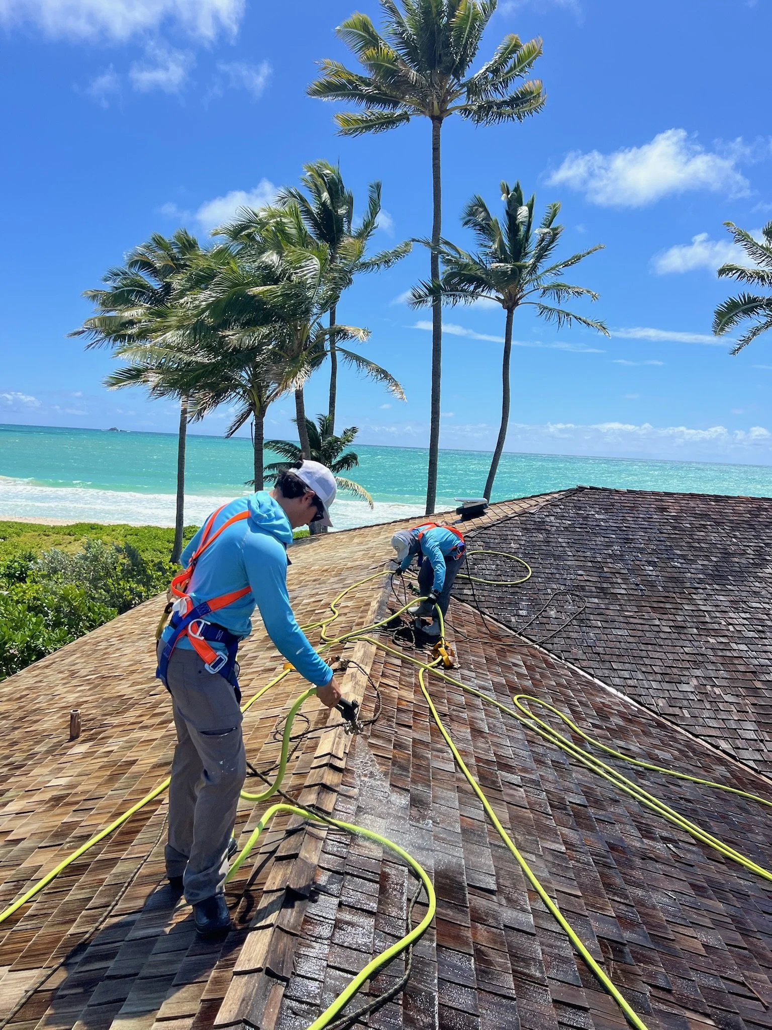 Person applying white waterproofing coating on flat roof with brush, buckets, and a sunny sky.