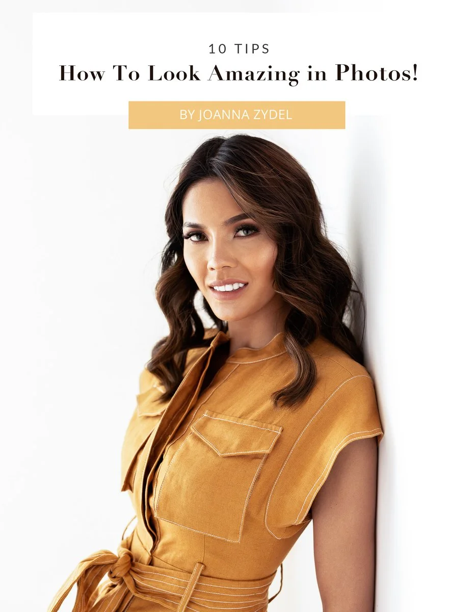 Cover of a guide titled '10 Tips How To Look Amazing in Photos!' by Joanna Zydel, featuring a woman with wavy brown hair wearing a tan sleeveless top, smiling and leaning against a white wall.