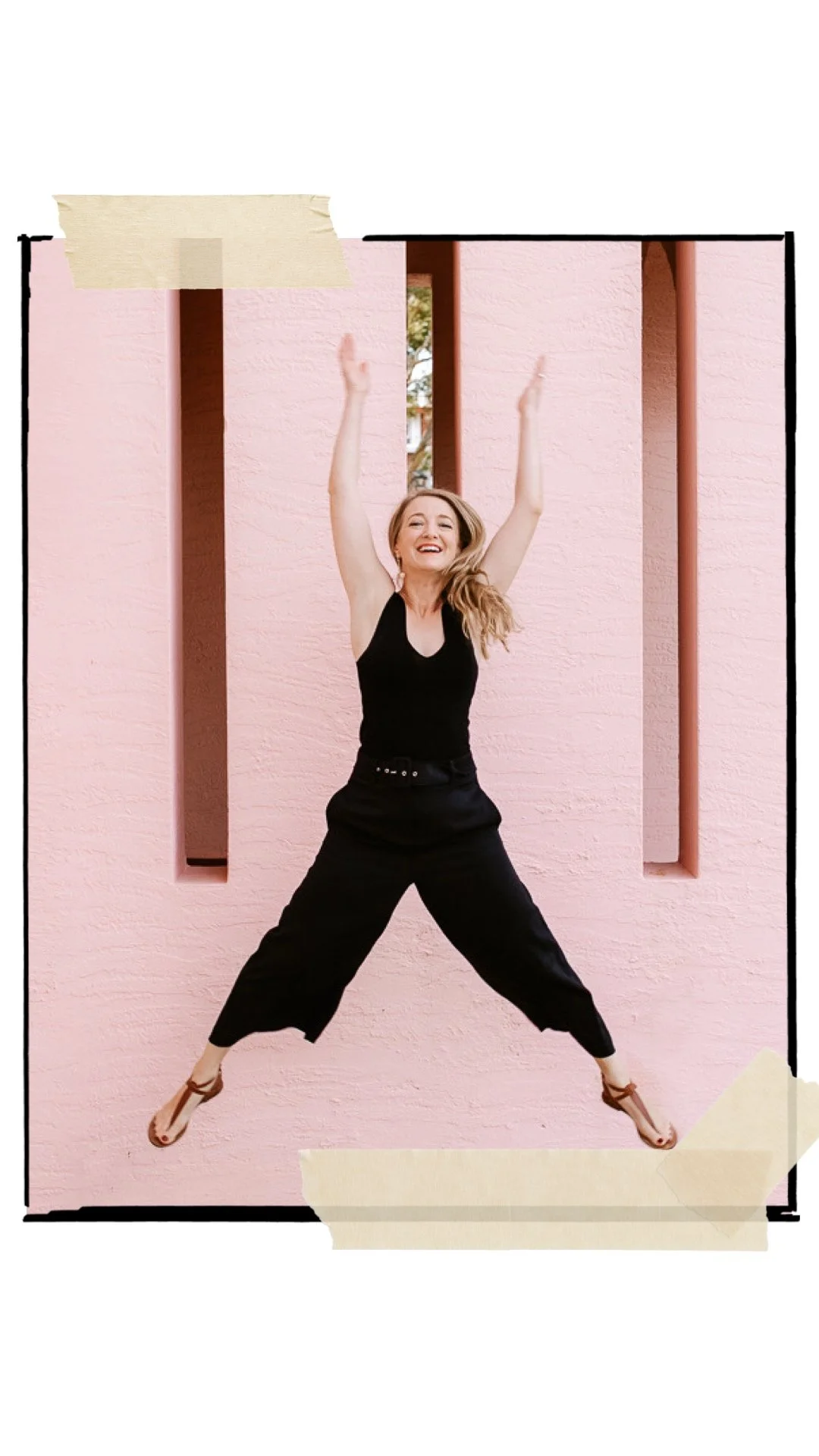 A woman jumping in the air with arms raised, wearing a black sleeveless top and black pants, in front of a pink textured wall with vertical narrow openings.