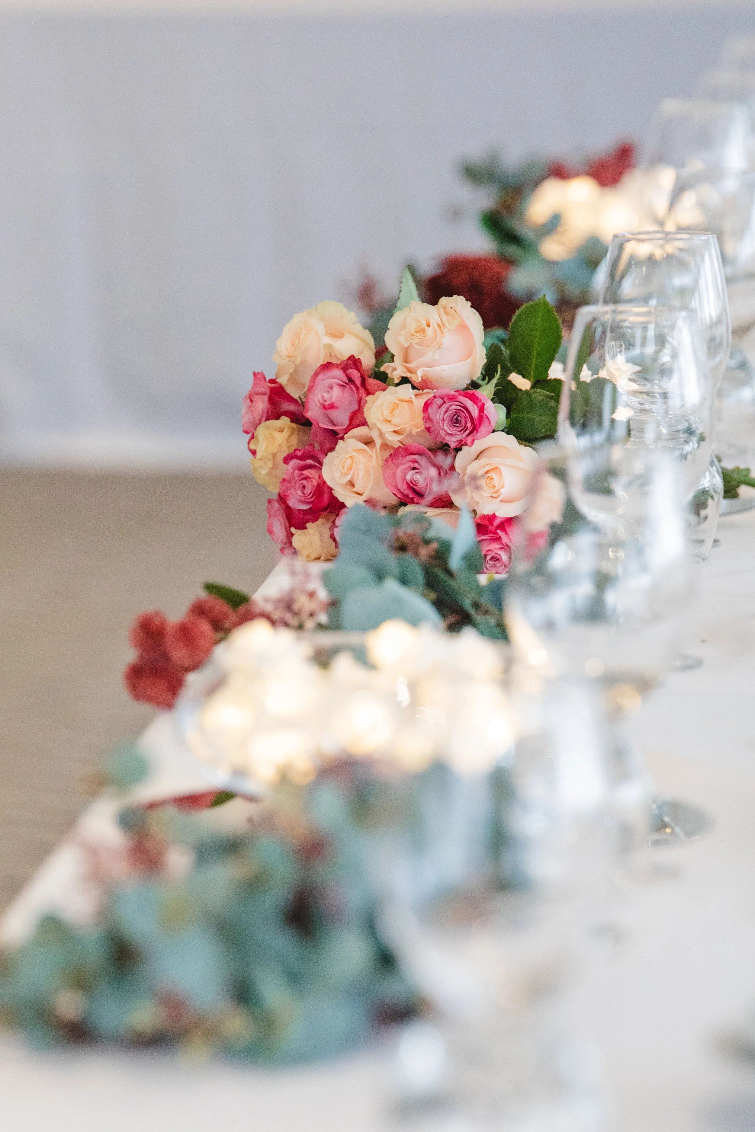 A floral centerpiece with pink and cream roses on a table with glassware.