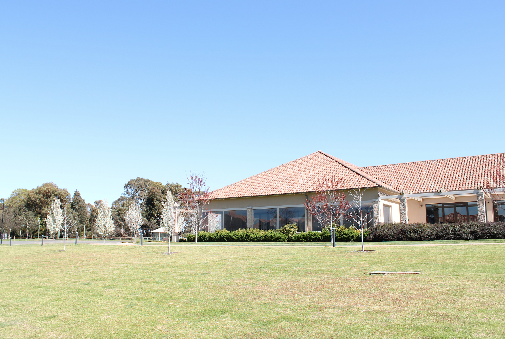 A building with a tiled roof surrounded by a grassy field, small trees, and bushes under a clear blue sky.