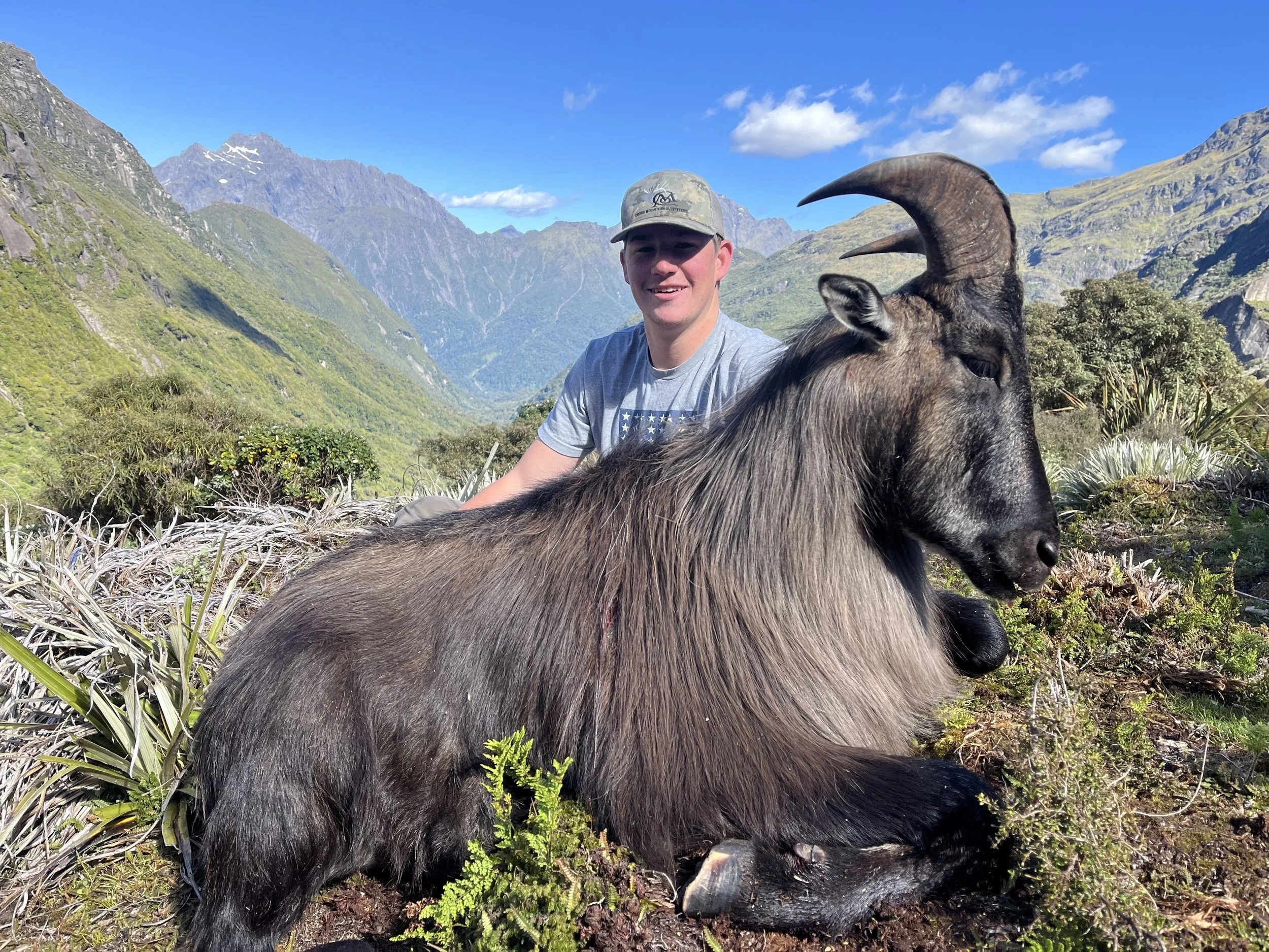 Trophy Bull Tahr with American hunter on hillside with the snowy Southern Alps in the background