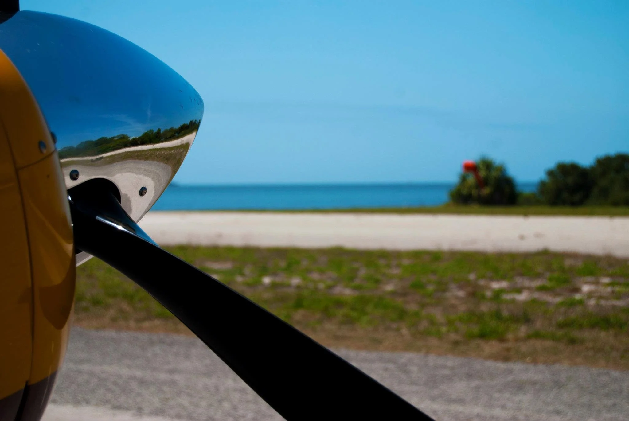 A planes propeller and spinner are visible in front of a runway. The runway is near the ocean.