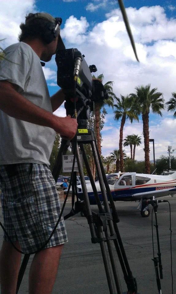 A television camera operator is seen shooting video of an airplane as it drives down a city street in Palm Springs, California