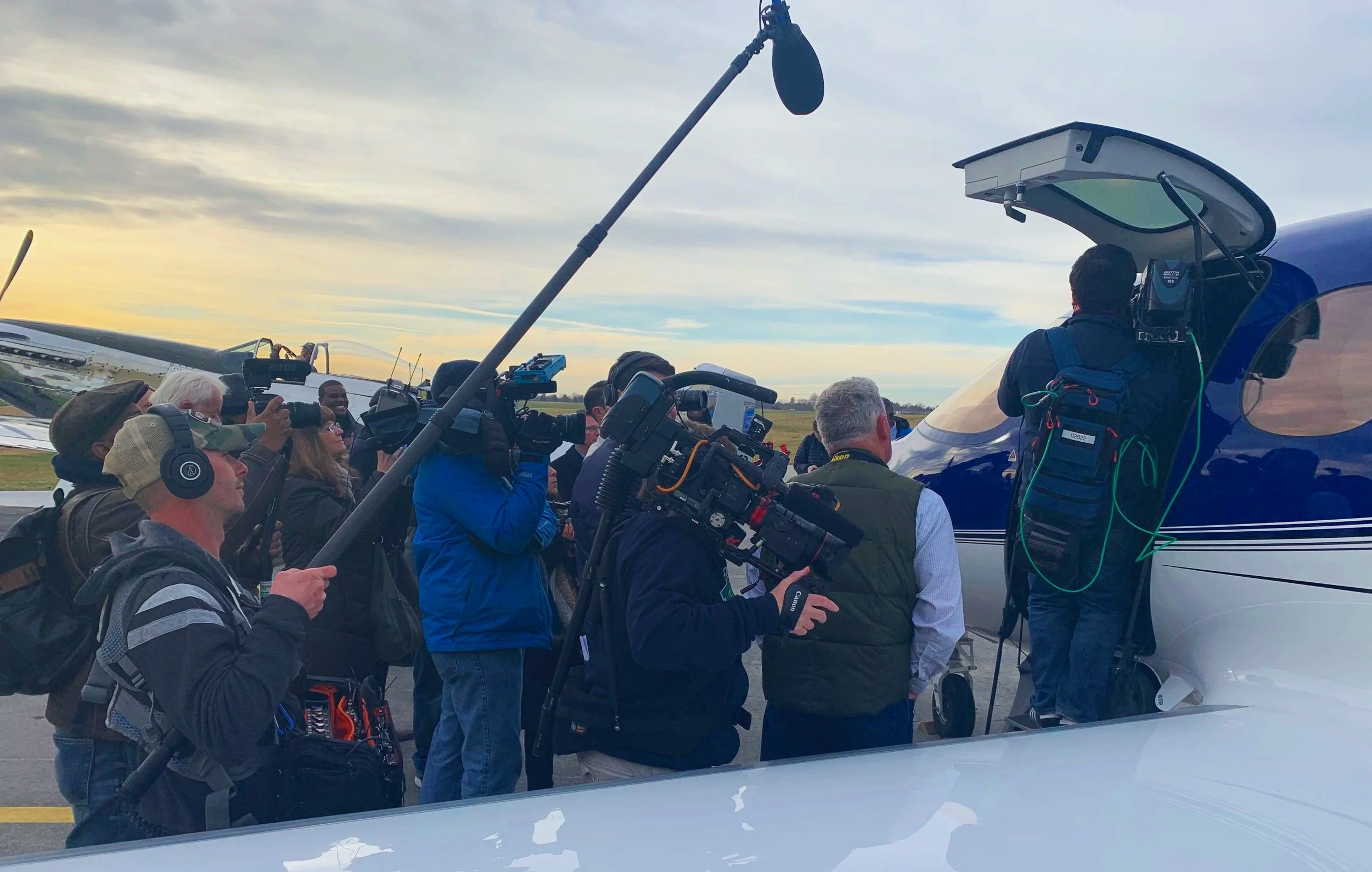A gaggle of media surround a Cirrus Vision Jet. A P-51 Mustang is seen in the background.