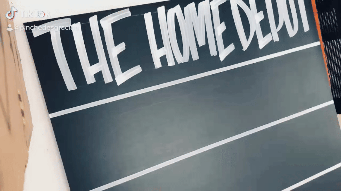Hand-painted black MDF sign with white hand-lettered text reading "The Home Depot," created for operational communication during COVID-19.