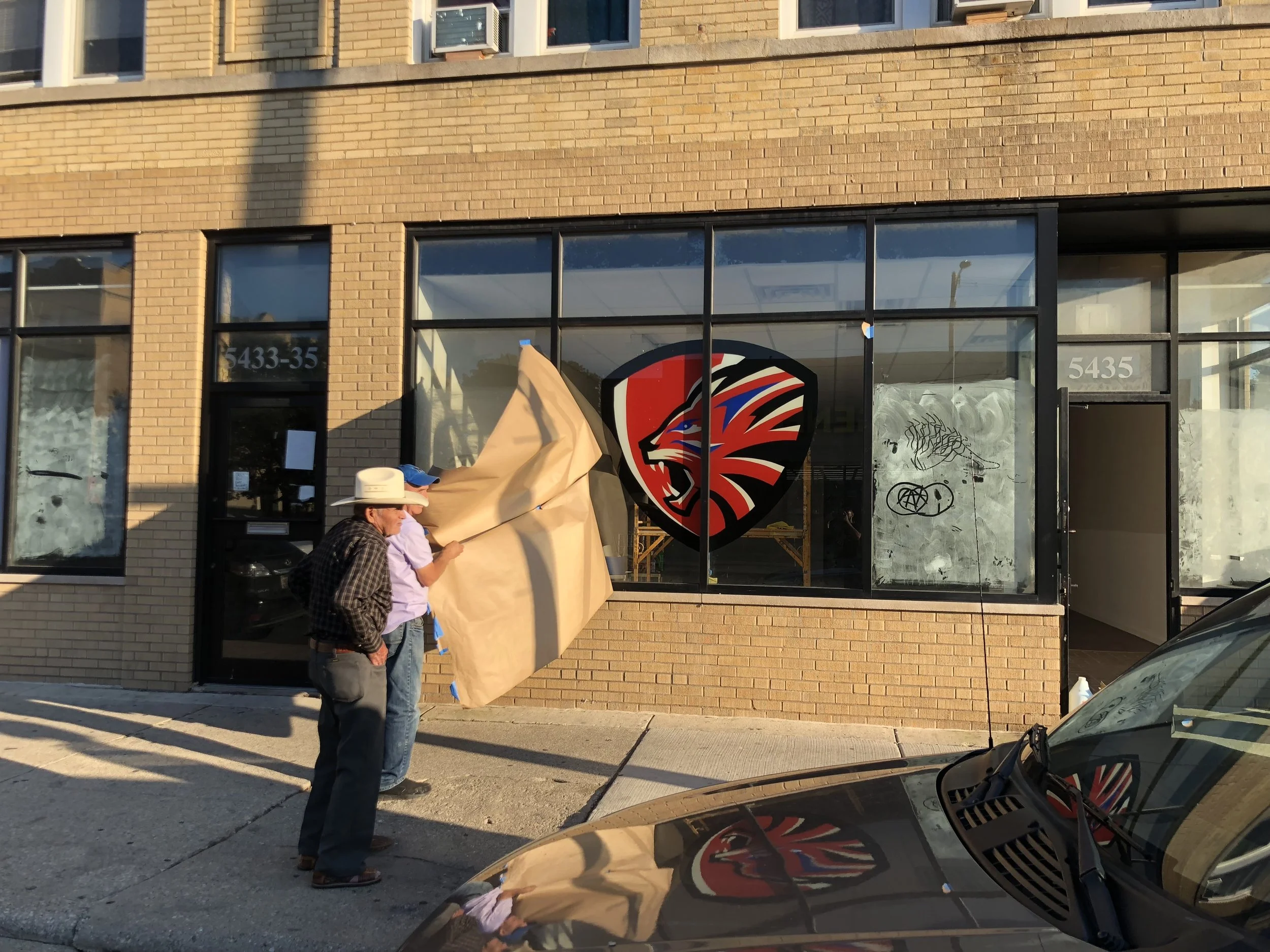 Hand-painted lion logo on a Chicago storefront window for Eat or Be Eaten Inc., created by DiverCity Artistry as a painted brand presence instead of vinyl.