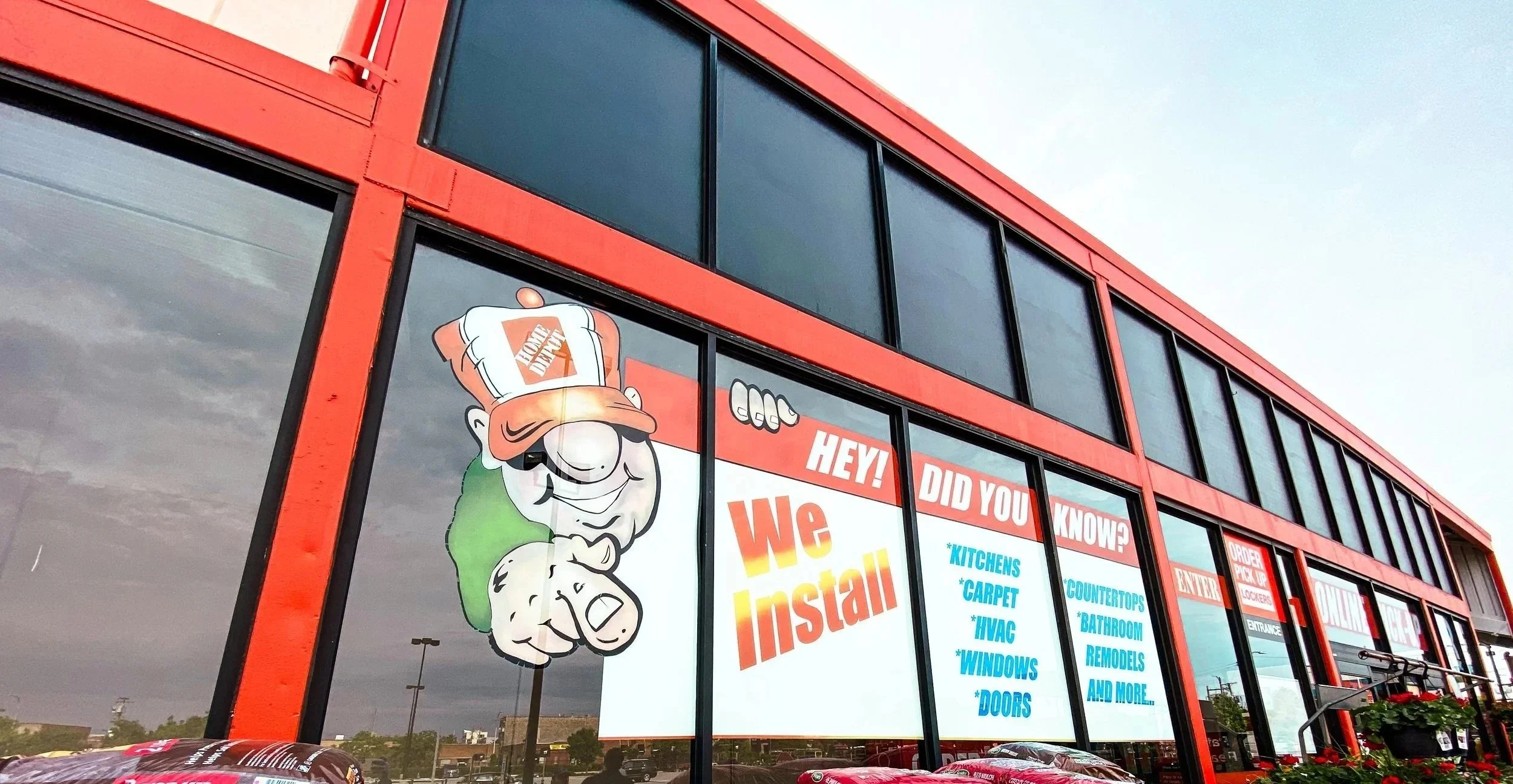 Hand-painted "We Install" window graphics featuring Home Depot's Homer character at the North Avenue flagship Home Depot in Chicago, created without vinyl using spray paint and acrylic by DiverCity Artistry.