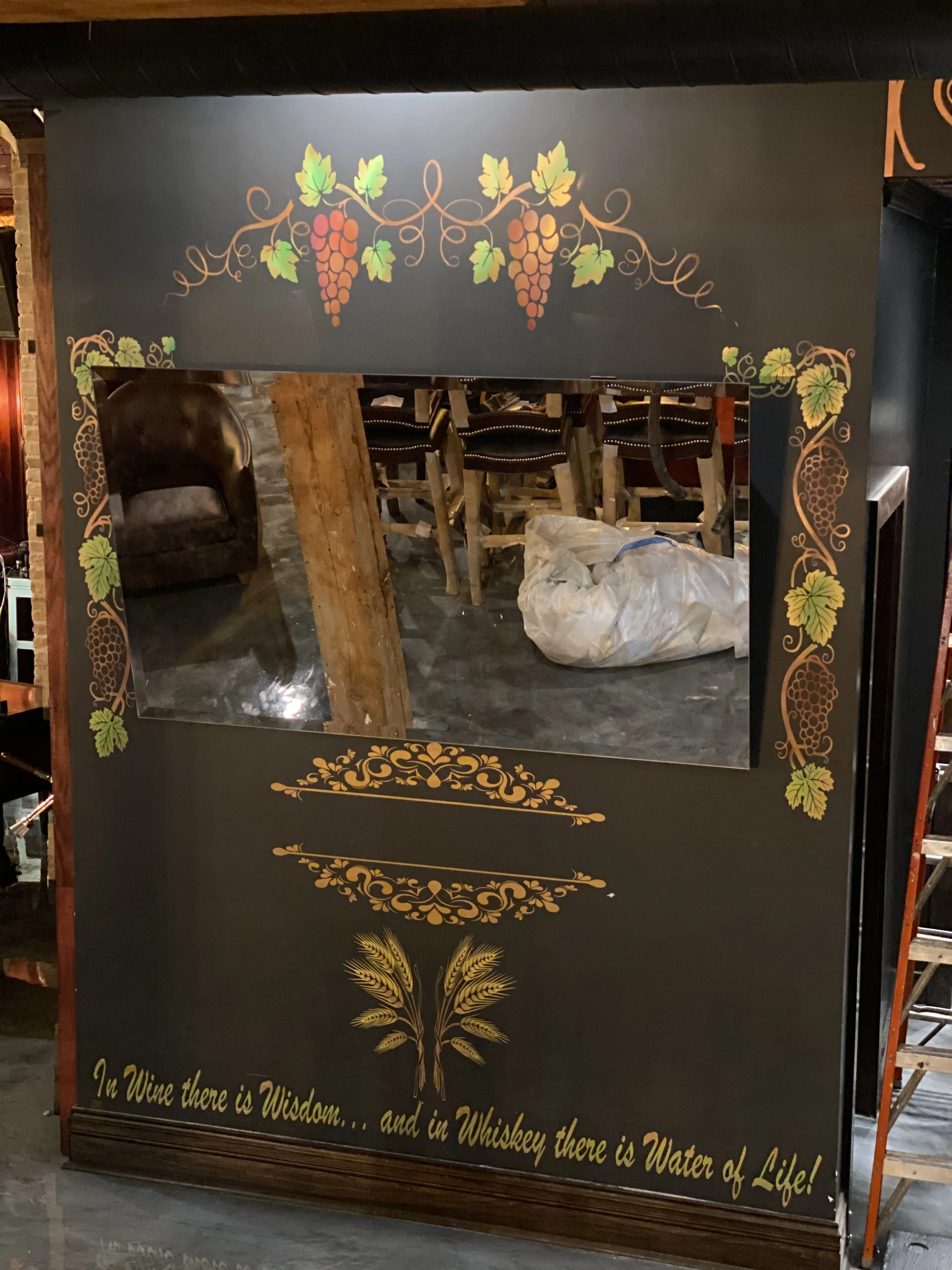 Custom hand-painted branded mirror display created for Grapes & Grains in Chicago using brushwork, airbrushing, spray finishing, and CNC-cut masking for premium hospitality branding by DiverCity Artistry.