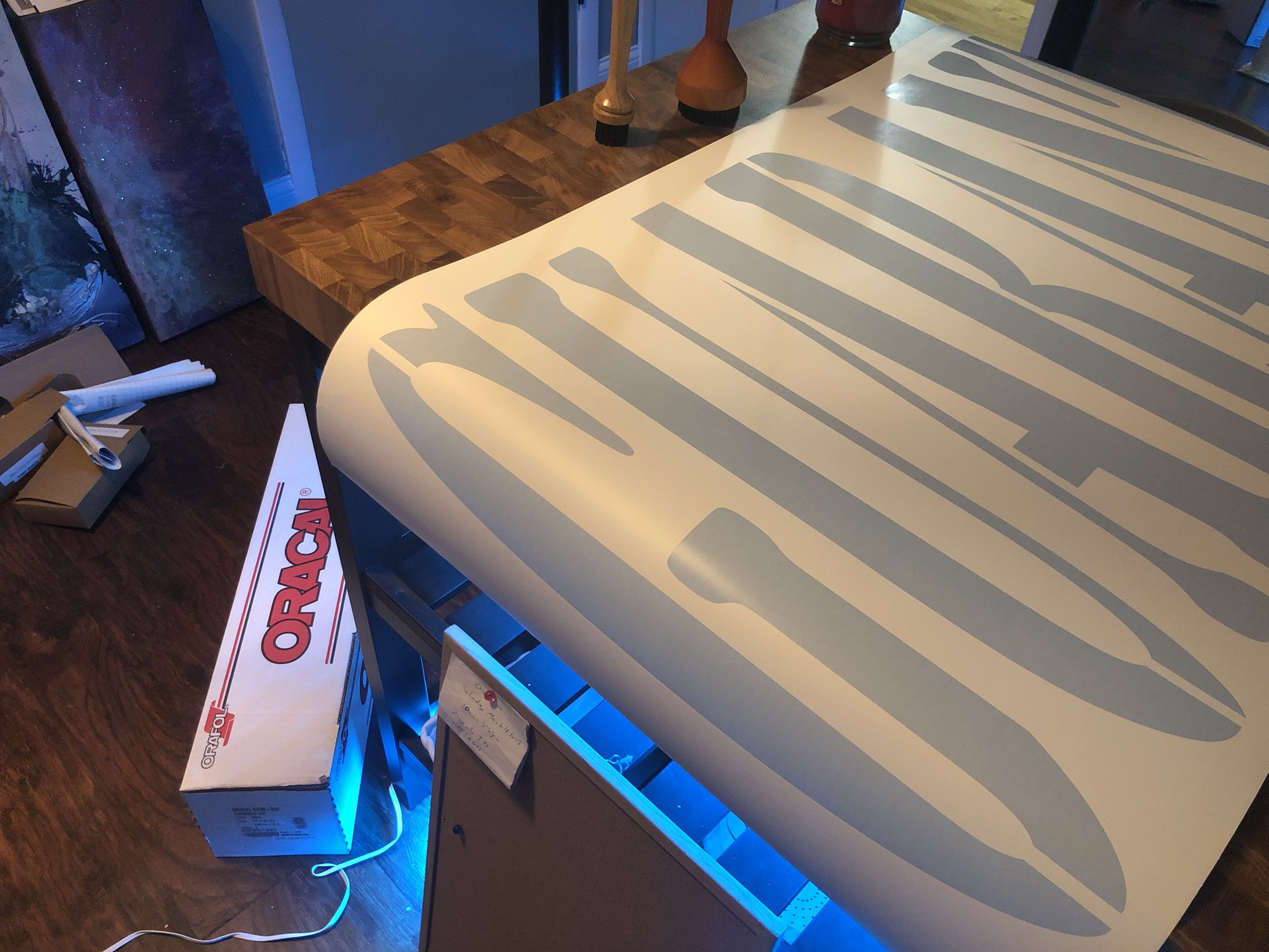 A large beige sign with the word 'ORACLE' cut out and illuminated from behind, sitting on a table. Nearby are a box labeled 'ORACLE' and some rolled-up posters or papers.