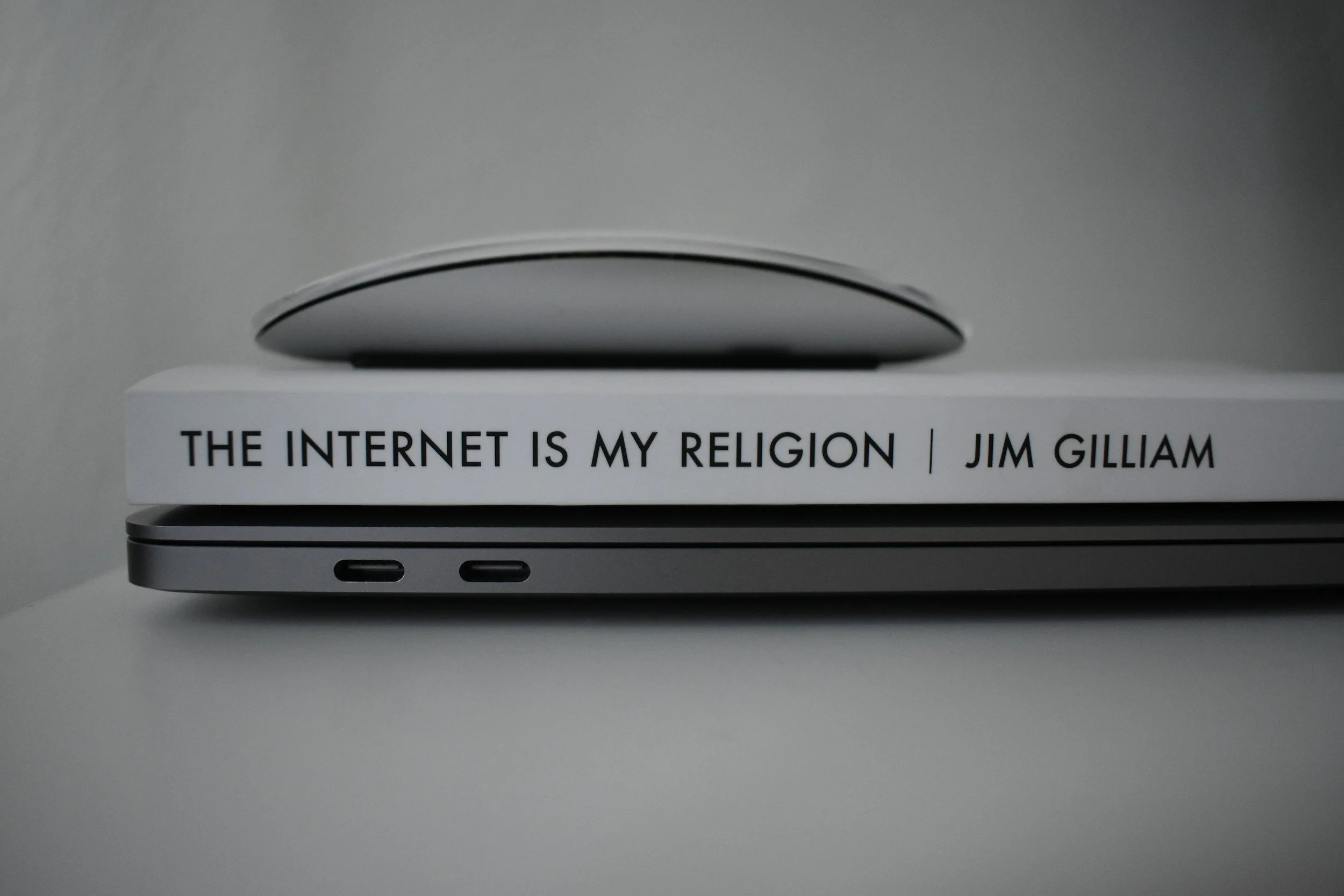 本の上に置かれたパソコンの横にある本のタイトルは『THE INTERNET IS MY RELIGION』と著者の名前はJIM GILLIAM。