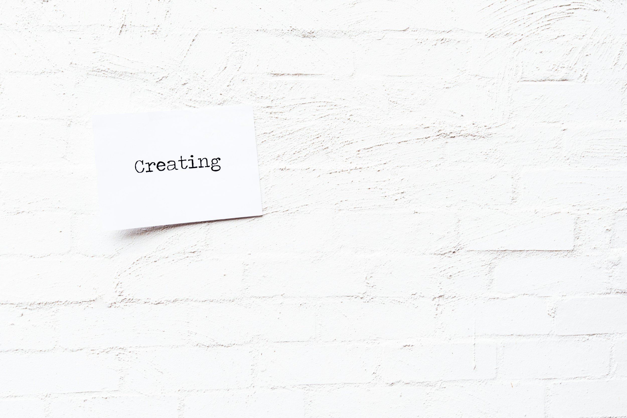 白いレンガの壁に貼られた紙に「Creating」と書かれている