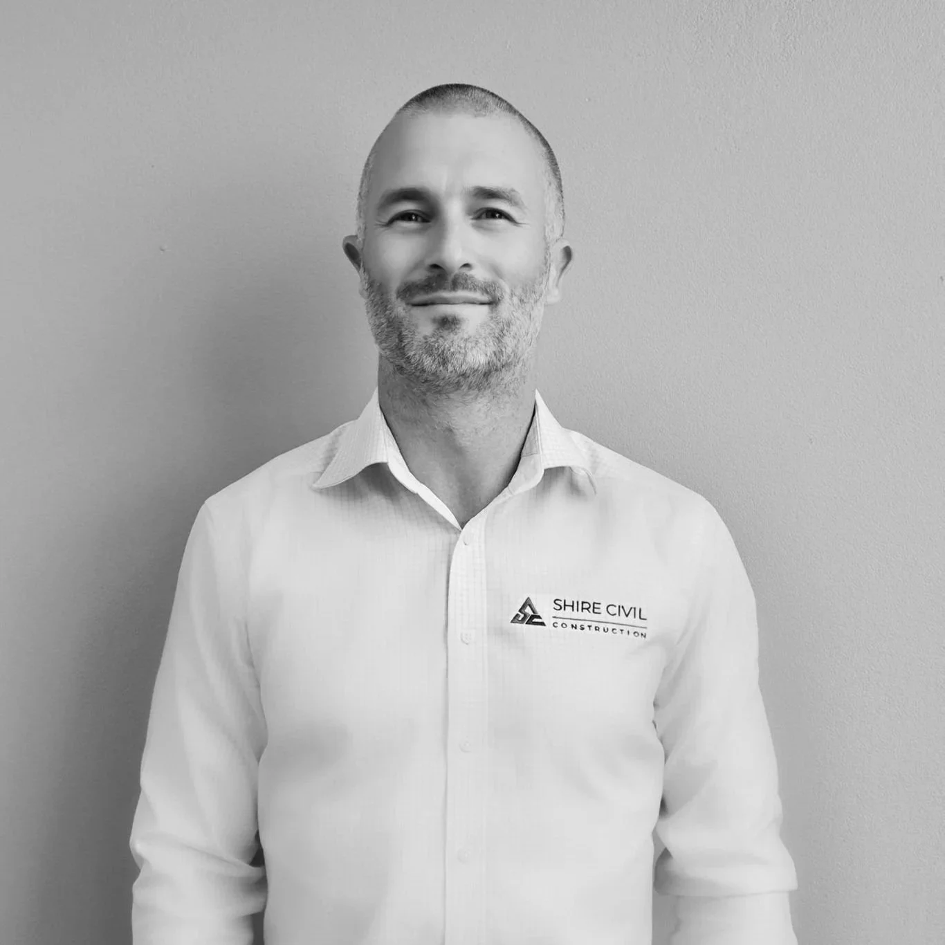 Black and white photo of a young man with curly hair, wearing an open white shirt, looking at the camera.