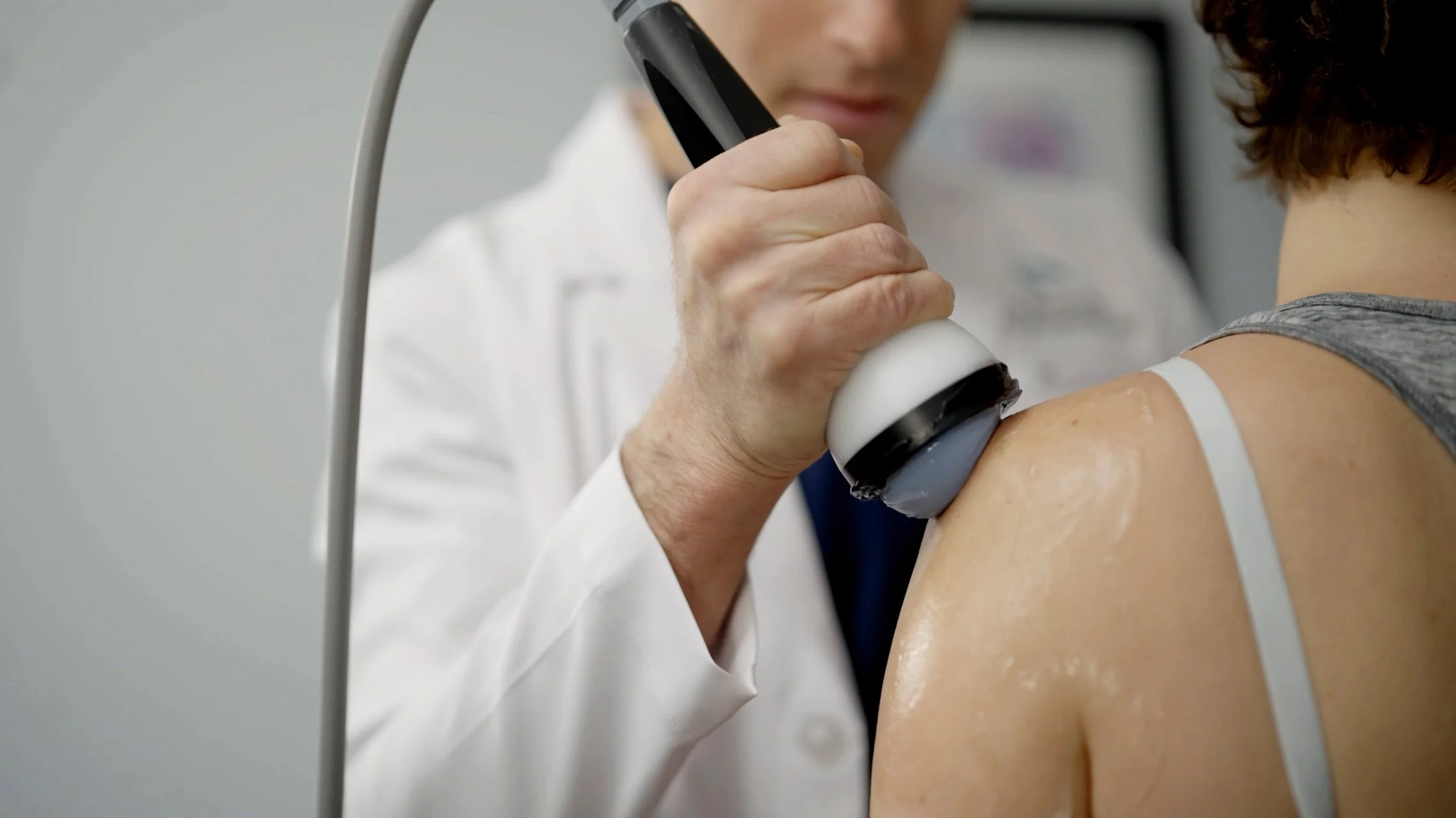A healthcare professional using a StemWave device on a patient's shoulder in a medical setting.