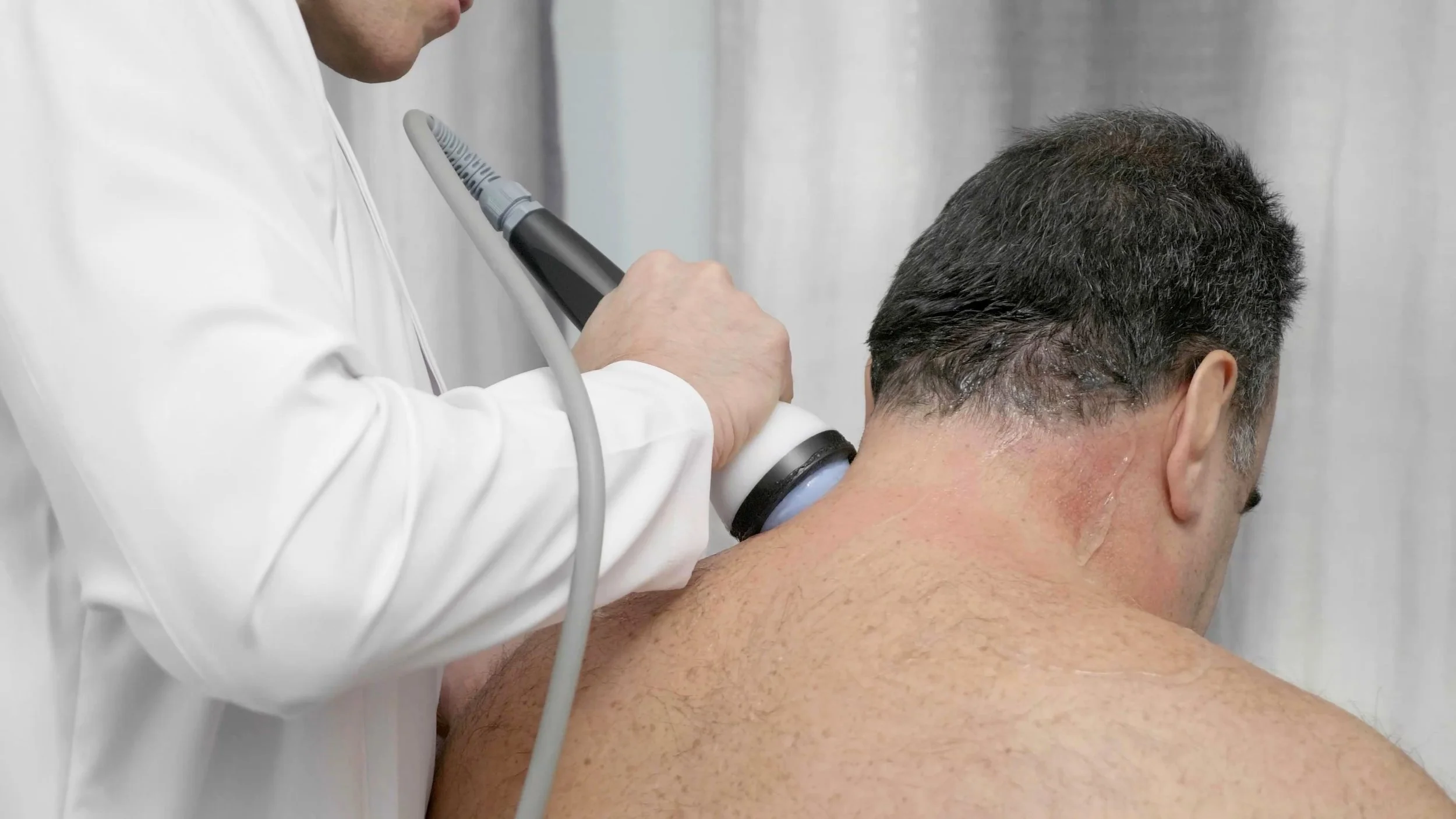 Doctor examining a man's neck with StemWave equipment.