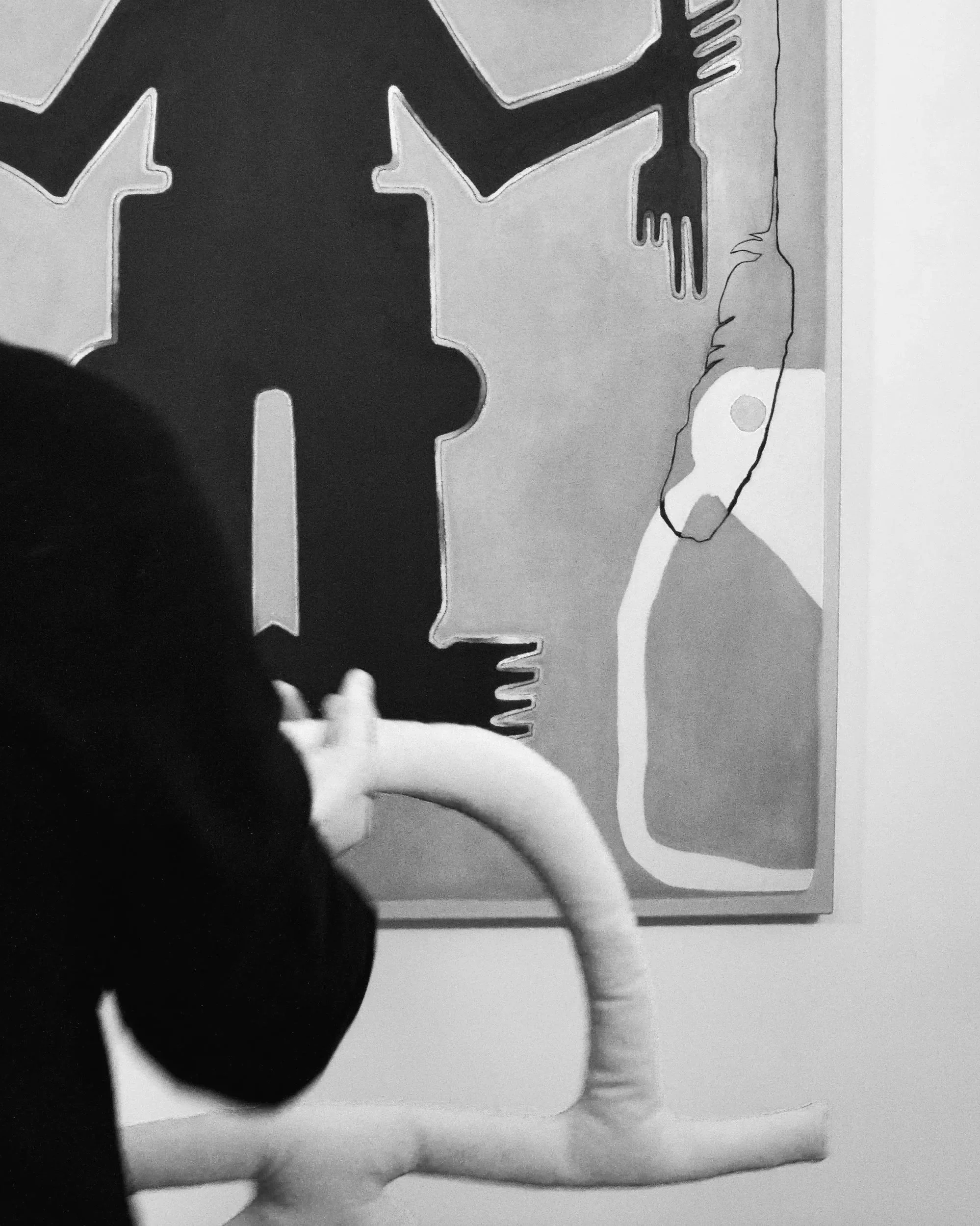 Person interacting with an art installation that includes a large black silhouette of a tree and a white, curvy sculpture resembling an abstract animal or creature.
