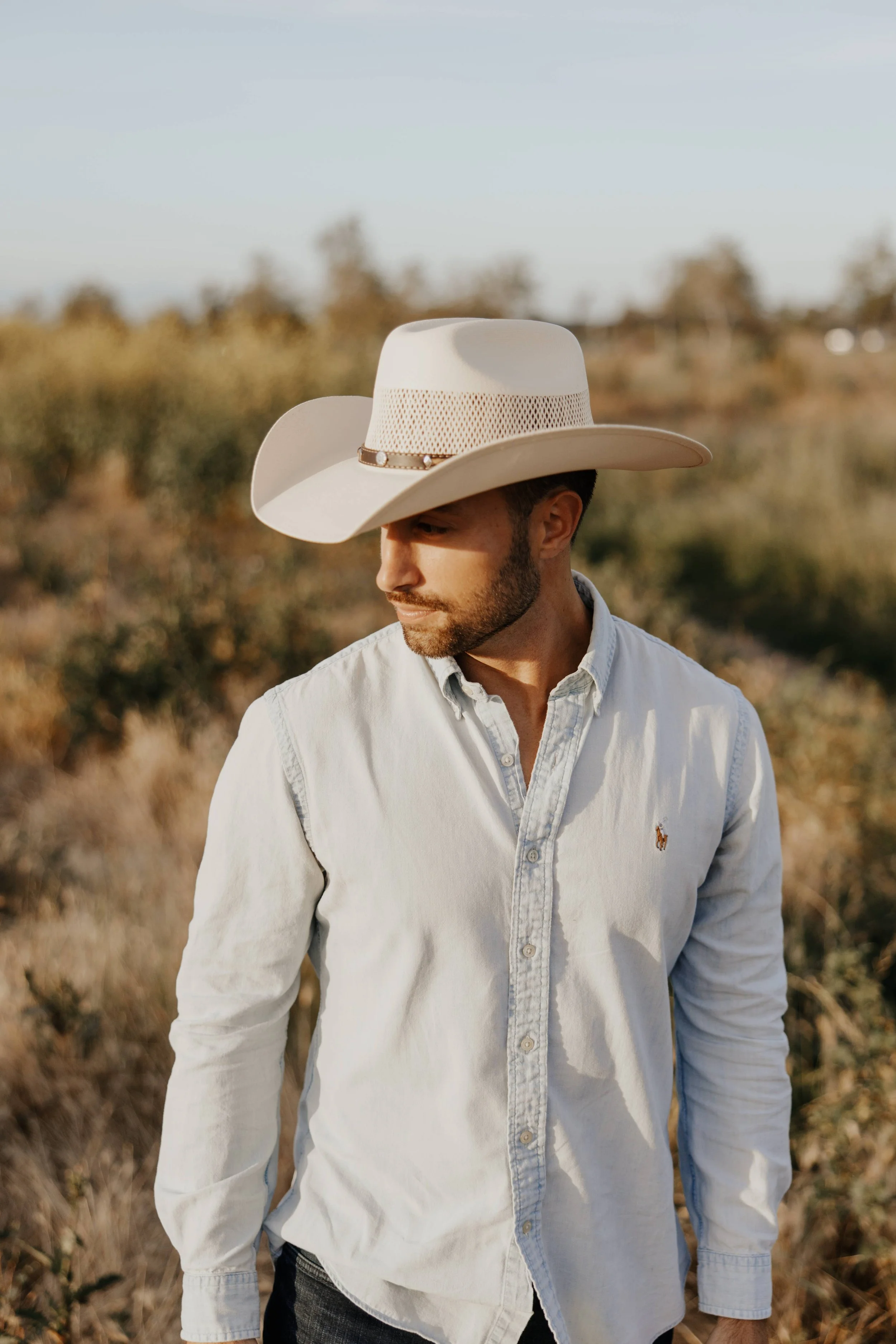 Man wearing a white shirt and light-colored cowboy hat outdoors.